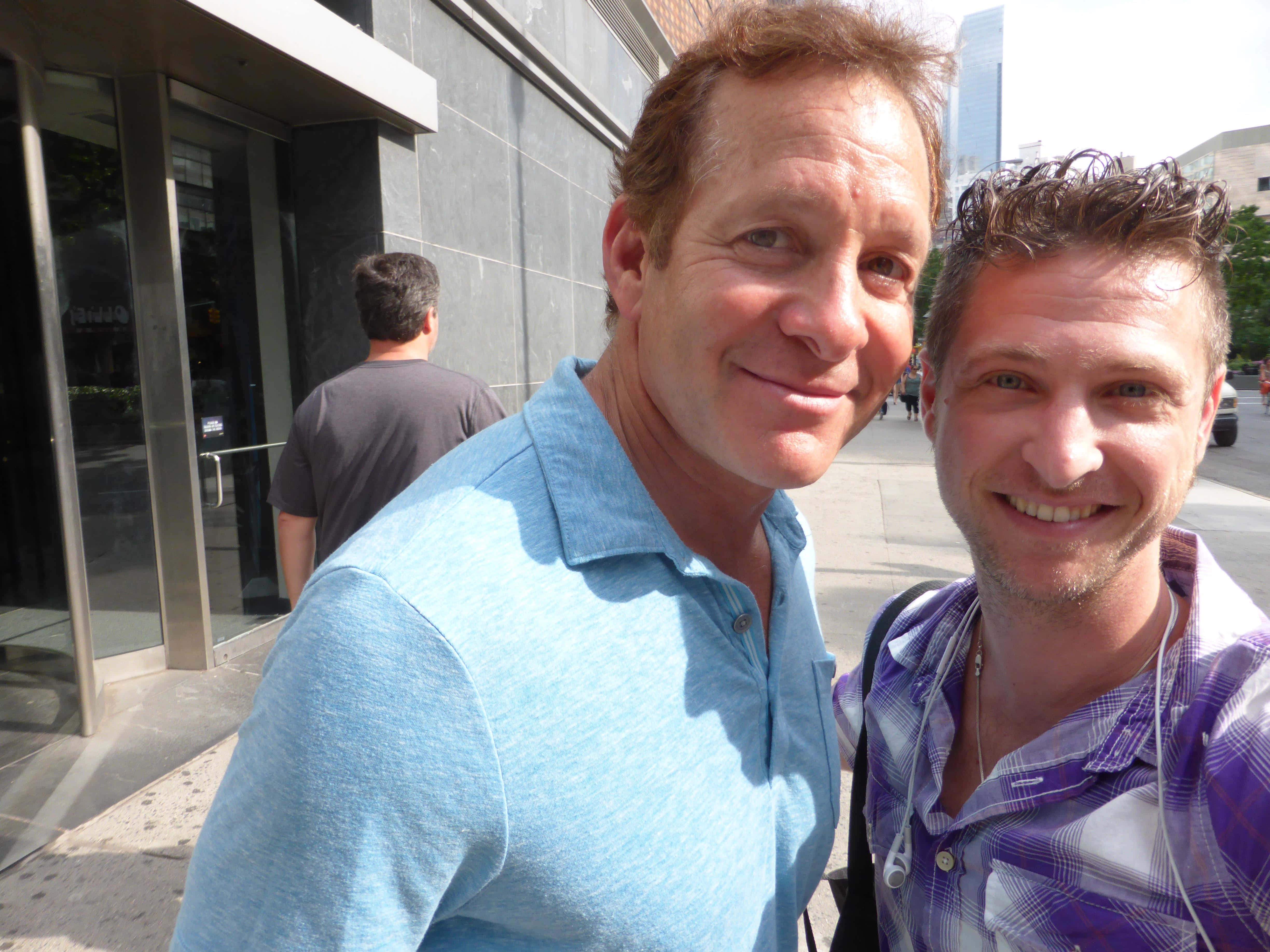 Steve Guttenberg 桌布 壁紙 — 兩位微笑嘅男士喺陽光普照嘅城市行人路上，喺現代玻璃建築入口附近自拍。