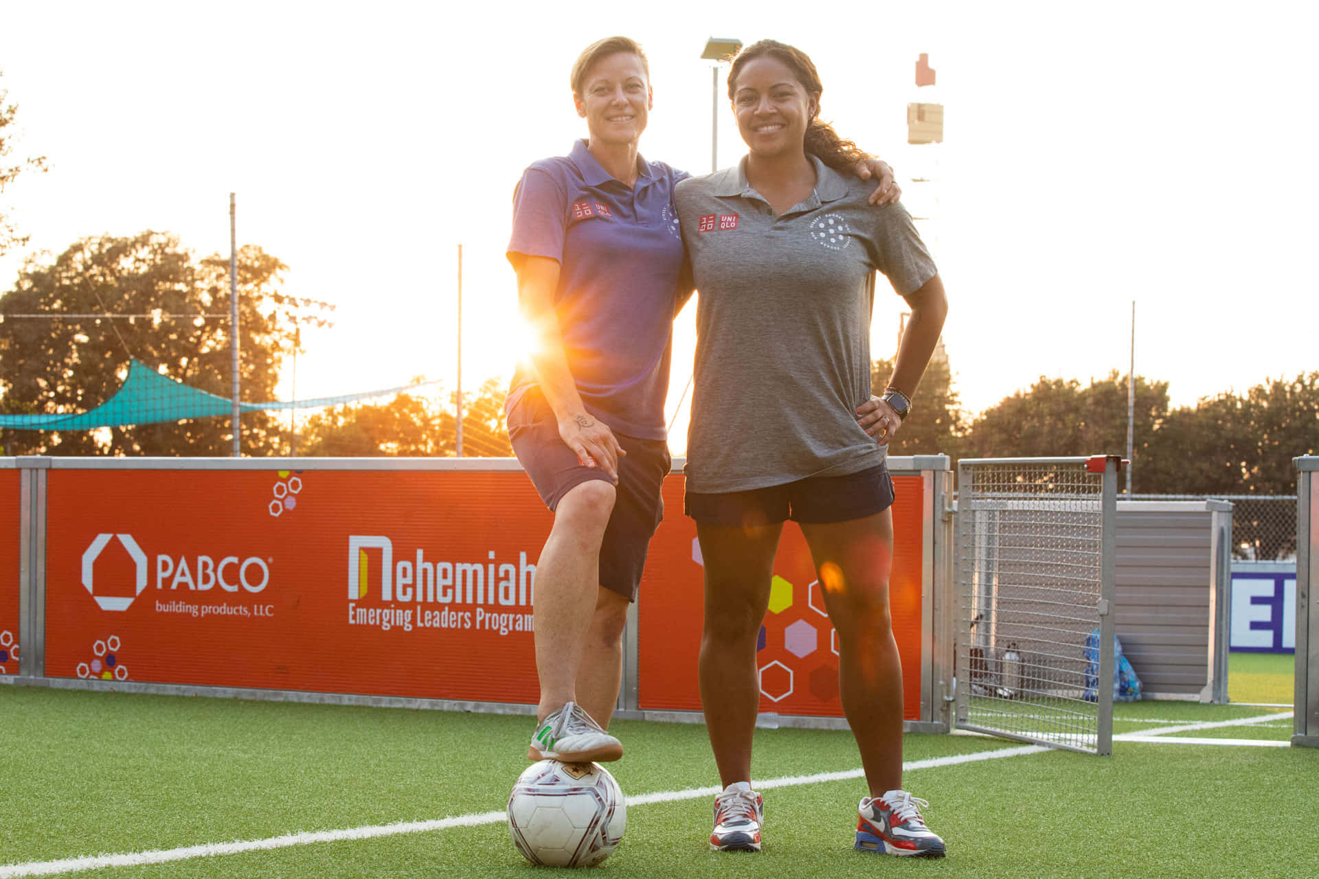 Street Soccer 桌布 壁紙 — 兩位微笑的女性在日落時分的足球場上擺姿勢，其中一位在球上保持平衡。