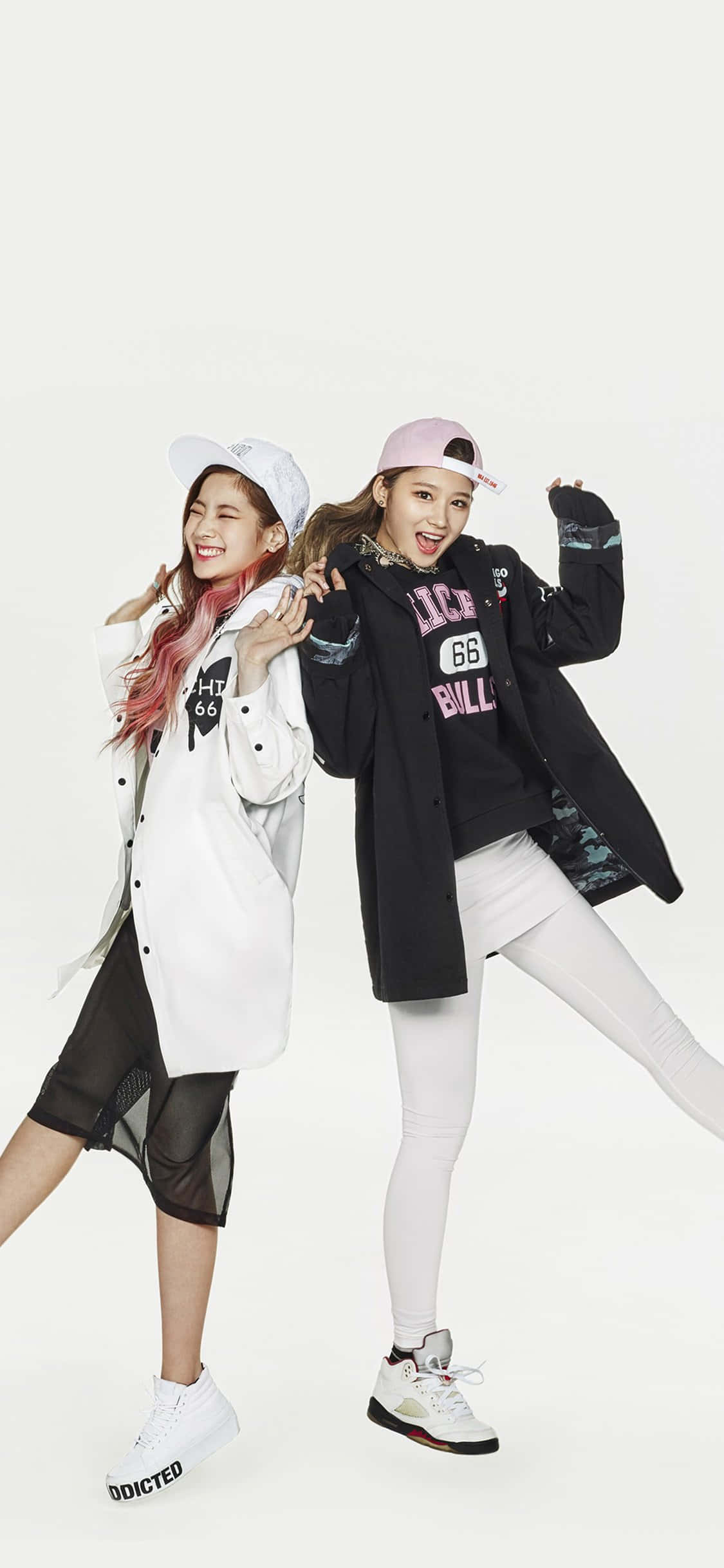 Kpop Kawaii 桌布 壁紙 — 兩位微笑的年輕女性穿著時尚街頭服飾，在純白背景前擺出俏皮姿勢。