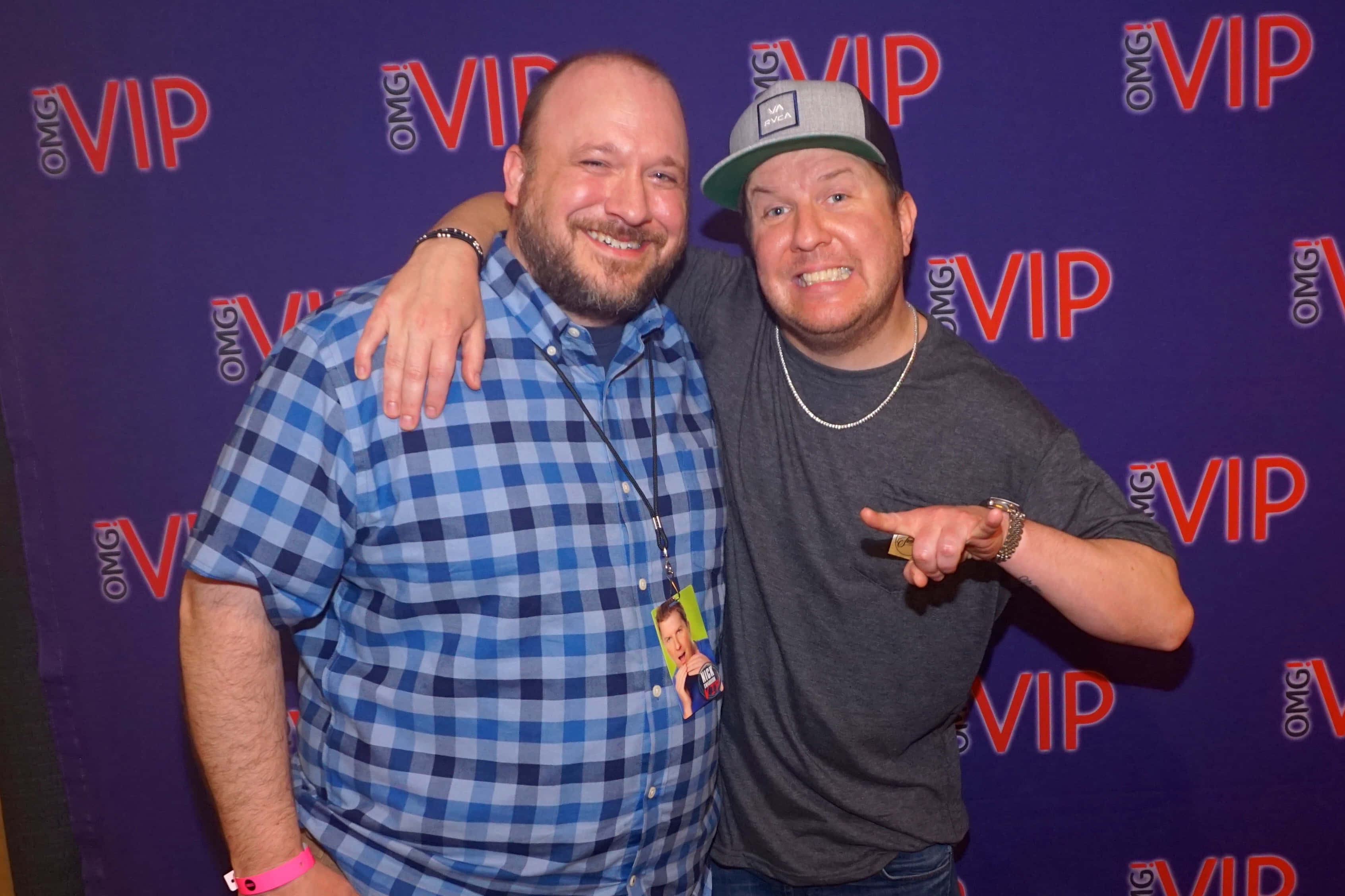 Nick Swardson 桌布 壁紙 — 兩位微笑的男士在VIP活動中一起擺姿勢，背景為紫色，帶有重複的紅色和白色標誌。