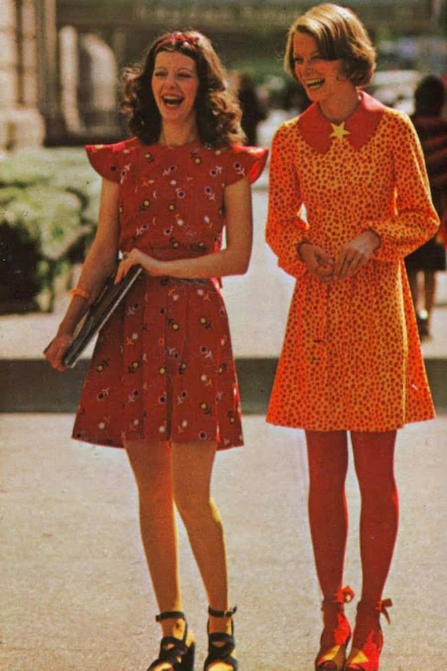 70年代gif 桌布 壁紙 — 兩位快樂的女性穿著充滿活力的1960年代花卉和圓點連衣裙，在陽光明媚的日子裡笑著走在戶外。