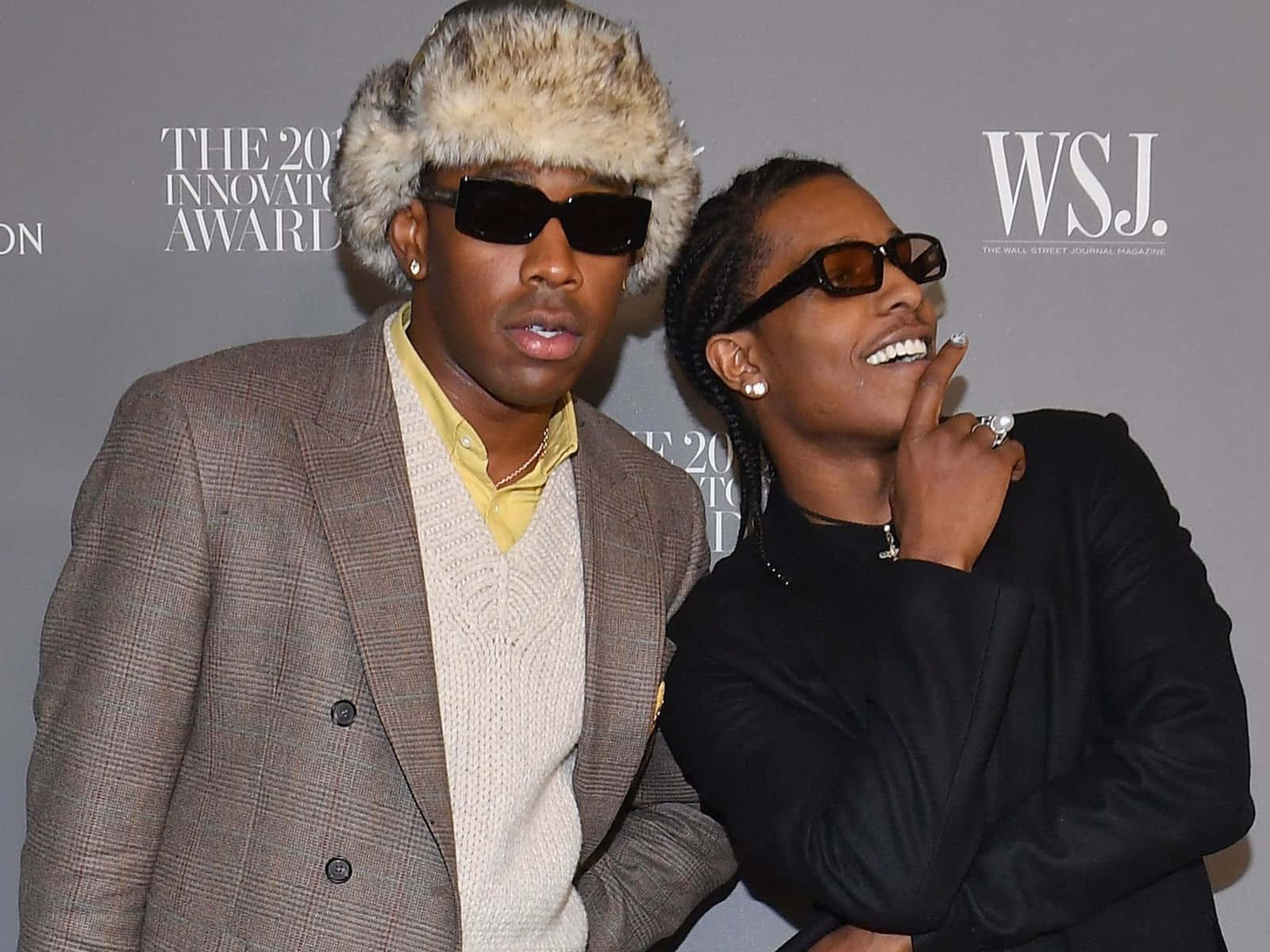tyler the creator 桌布 壁紙 — 兩位時尚饒舌歌手在正式活動中自信地擺姿勢，戴著皮草帽和太陽眼鏡，背景為品牌標誌。