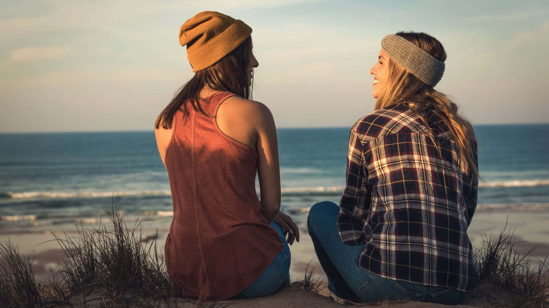 Best Friend 桌布 壁紙 — 兩位朋友並肩坐在沙丘上，俯瞰黃金時段的海洋，微笑著分享寧靜的時刻。