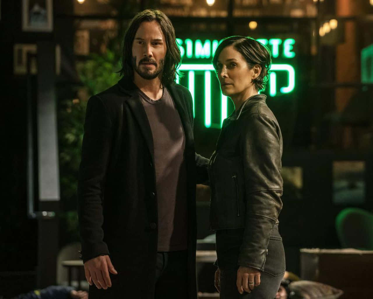 Keanu Reeves 桌布 壁紙 — 兩位演員站在昏暗的城市夜景中，背後有發光的綠色霓虹招牌。