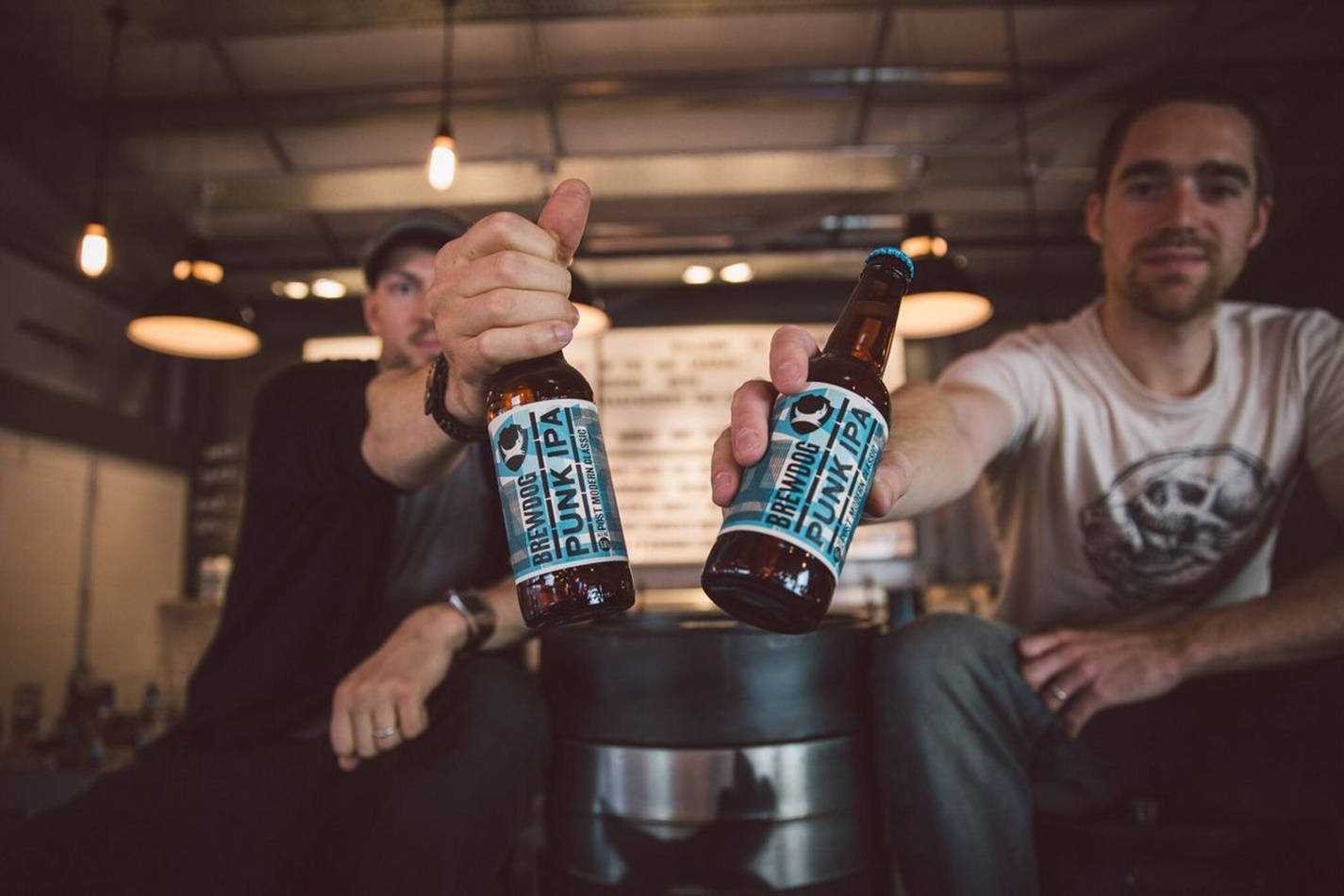 兩位男士手持 BrewDog Punk Ipa 瓶子 壁紙 — 兩個男人在燈光昏暗的酒吧裡碰著BrewDog Punk IPA啤酒瓶，豎起大拇指。
