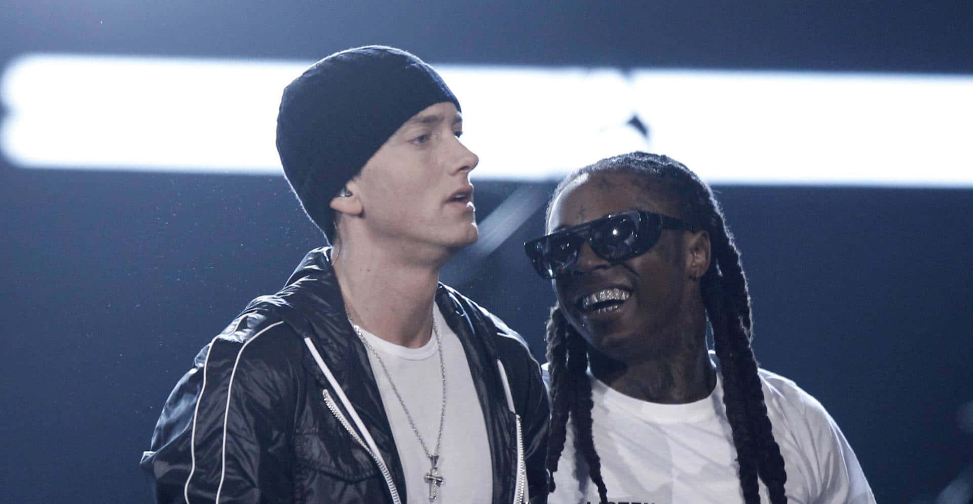 Eminem 桌布 壁紙 — 兩位說唱歌手在明亮燈光下的舞台上，一人戴冷帽，另一人戴太陽眼鏡，兩人均微笑