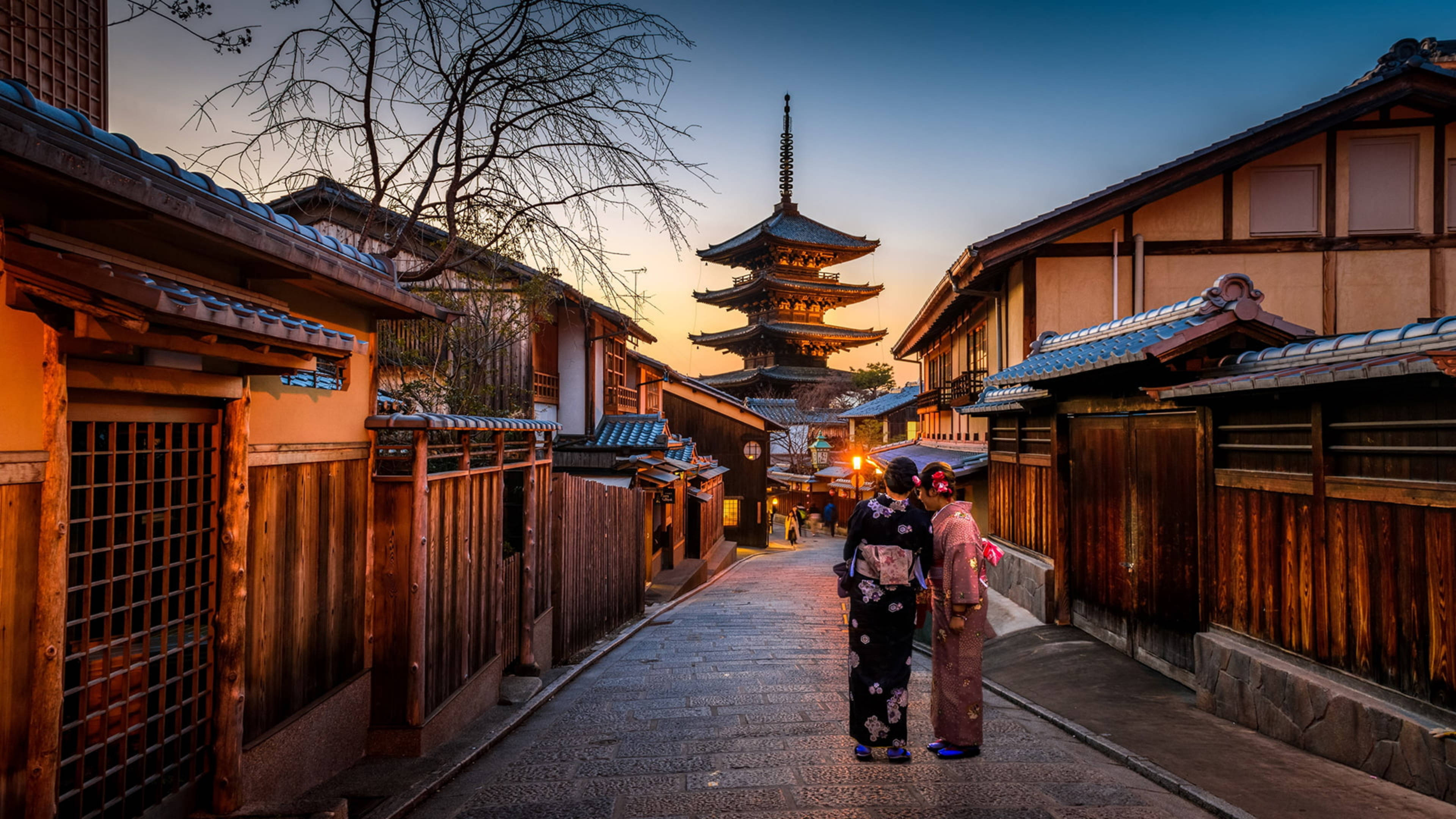 Japanese 桌布 壁紙 — 兩位身穿和服的女士在黃昏時分沿著狹窄的木巷走向一座寶塔。