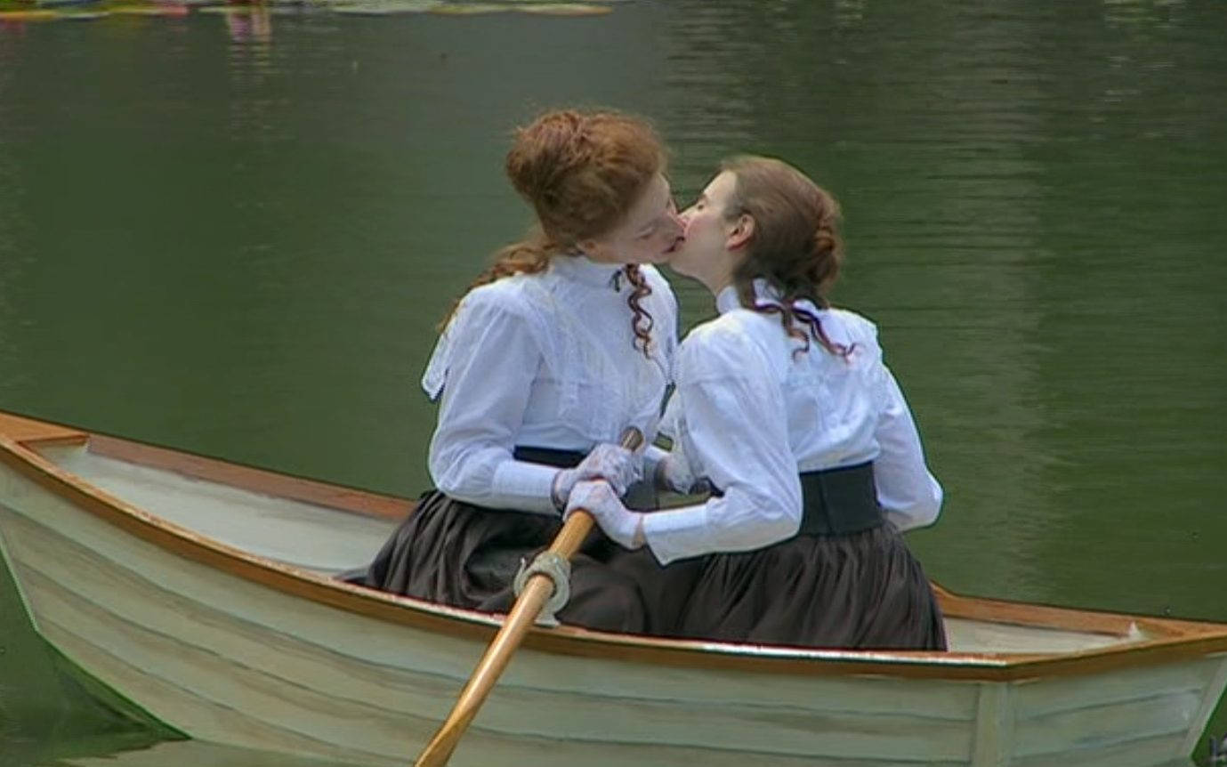 Edwardian Girls Kissing Art 壁紙 — 兩位身穿復古白襯衫和深色裙子的女性在平靜的綠色池塘上的木製划艇中溫柔地接吻。