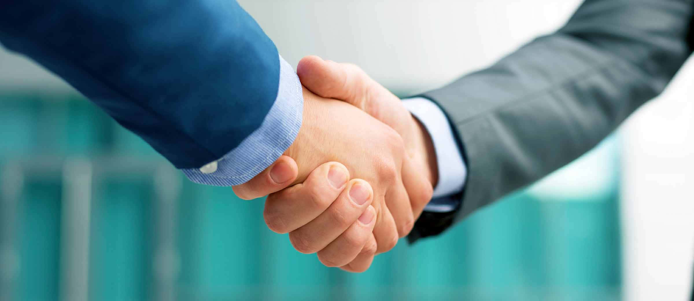 Sales 桌布 壁紙 — 兩位身穿西裝的商務人士在模糊的現代辦公室背景下堅定地握手。