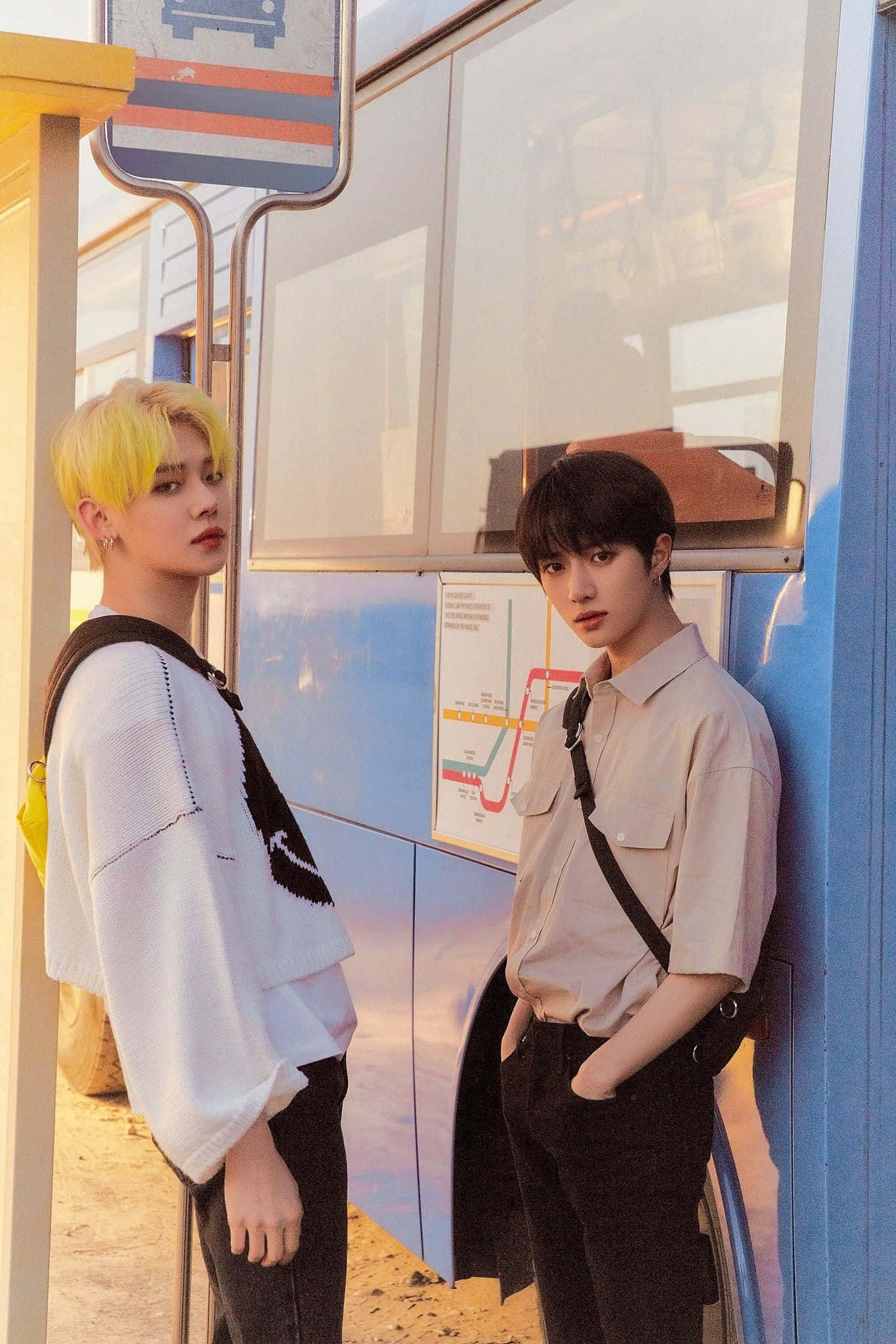 Big Hit Entertainment 桌布 壁紙 — 兩位髮型不同的年輕男子在溫暖的金色光線下站在色彩繽紛的巴士站。