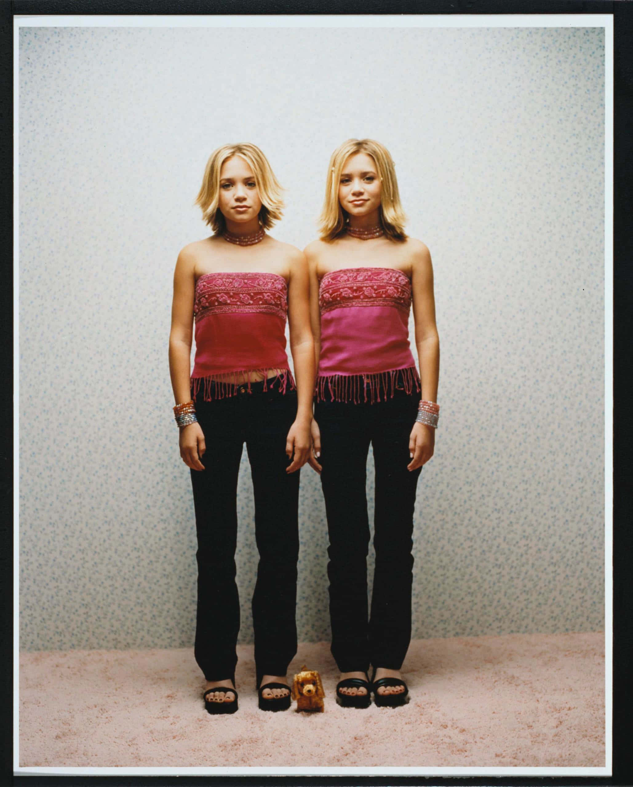 ashley olsen 桌布 壁紙 — 兩個一模一樣的雙胞胎女孩穿著相配的粉紅色流蘇上衣和黑色褲子，並排站在斑駁的牆壁前。