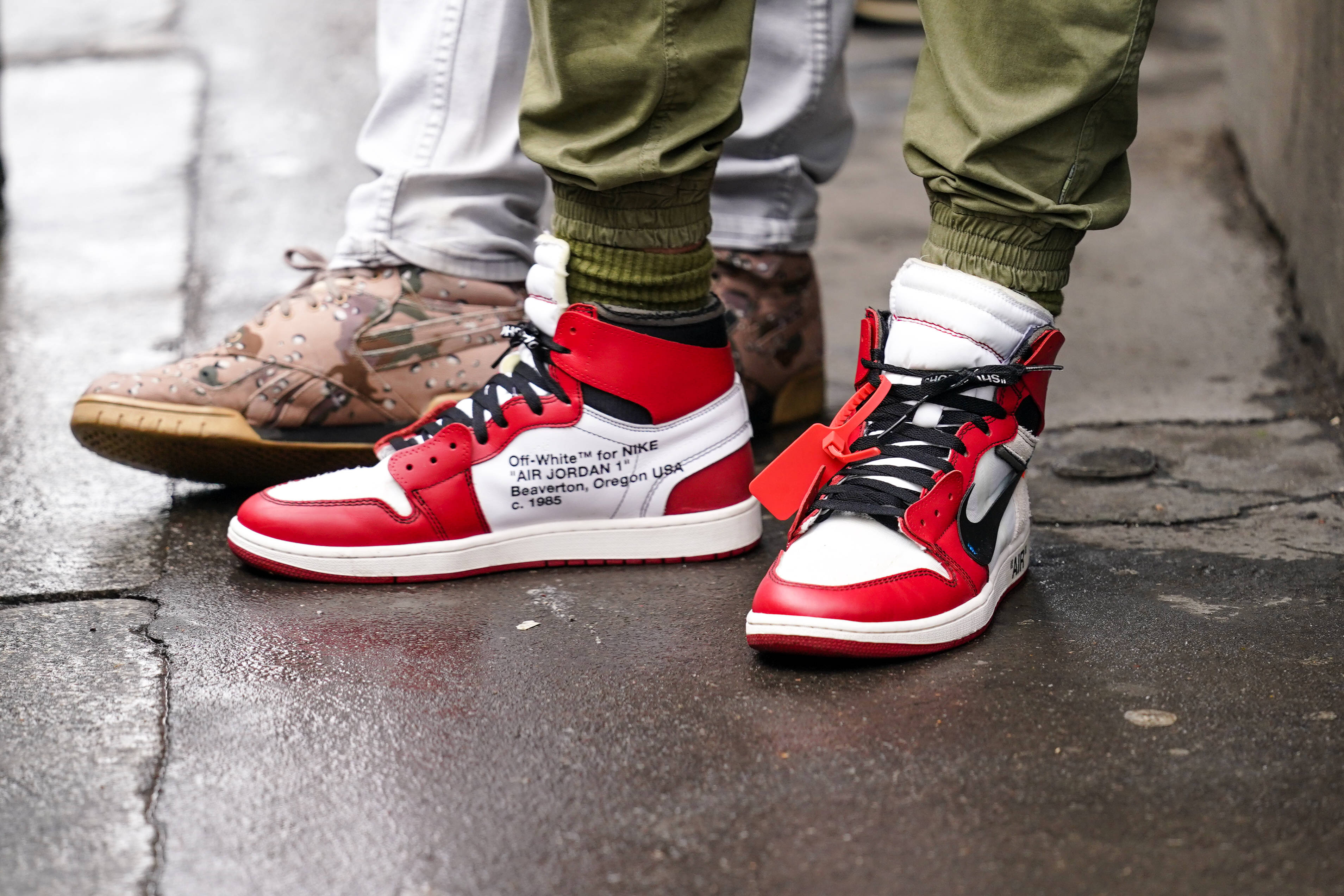 Nike Air Jordan 1 桌布 壁紙 — 兩個人嘅腳近距離特寫，著住紅、白、黑色運動鞋喺濕嘅城市行人路上。