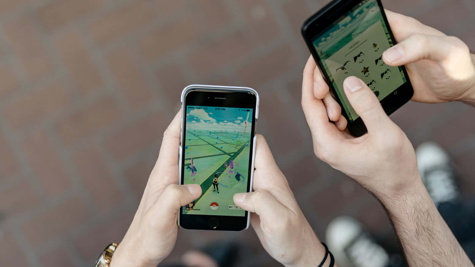 Pokemon Virtual World 桌布 壁紙 — 兩個人在戶外的磚砌路面上用智能手機玩Pokemon Go。