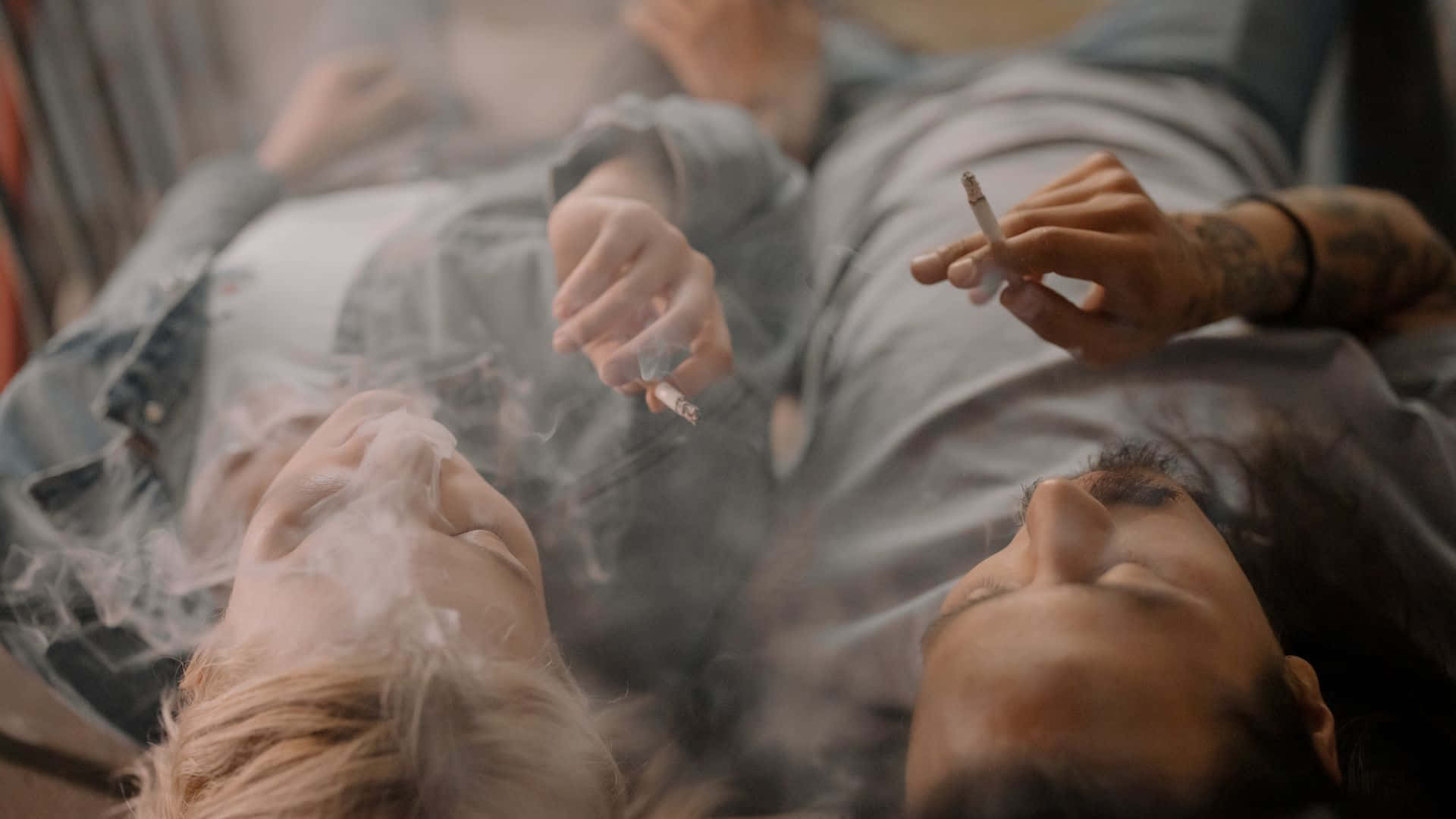 吸煙 桌布 壁紙 — 兩個人在昏暗的房間裡仰臥吸煙，煙霧在他們臉龐周圍繚繞。