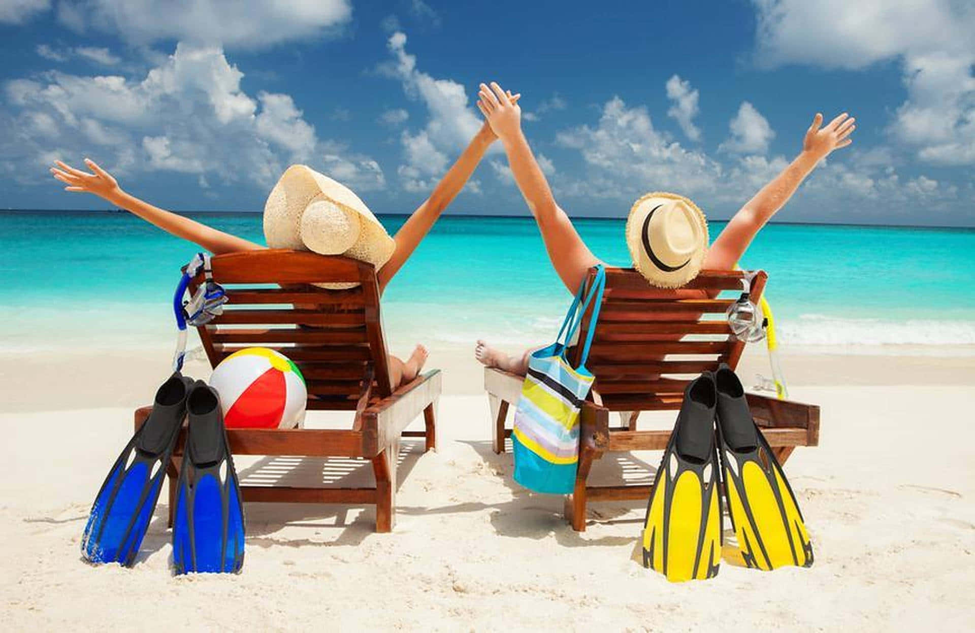 Beach Getaway 桌布 壁紙 — 兩個人在木製沙灘椅上放鬆，舉起手臂，在明亮的藍天下，附近有腳蹼和沙灘球。