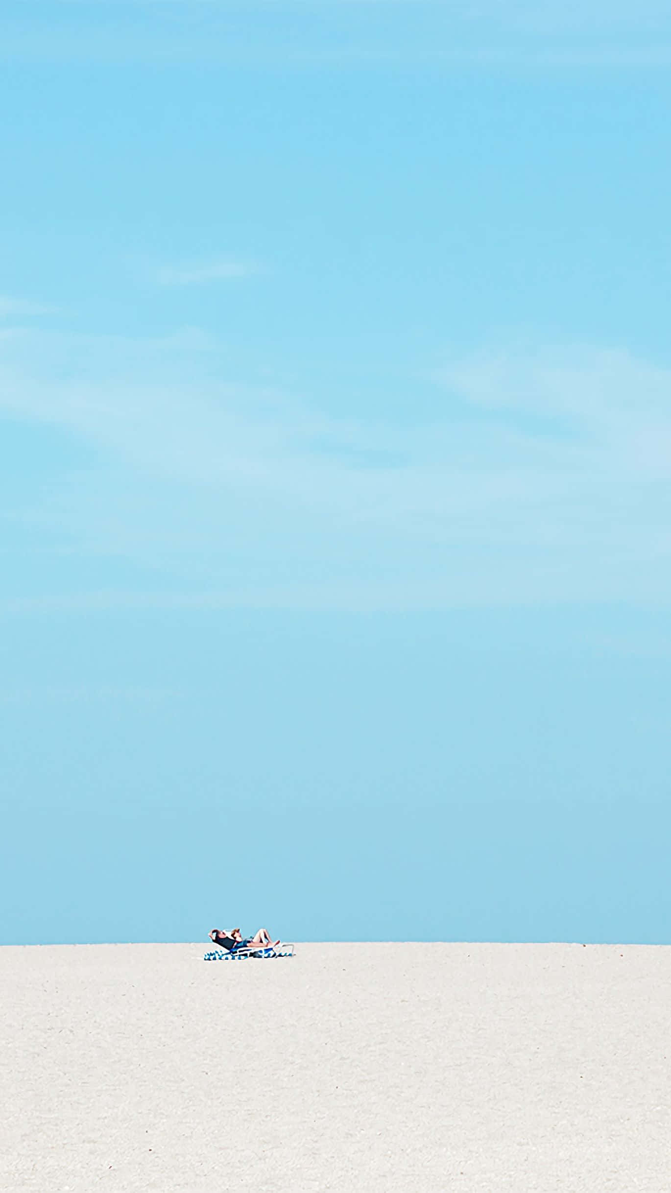 Minimalist Sky 桌布 壁紙 — 兩個人在藍色躺椅上放鬆，身處廣闊的白色沙漠，頭頂清澈藍天。
