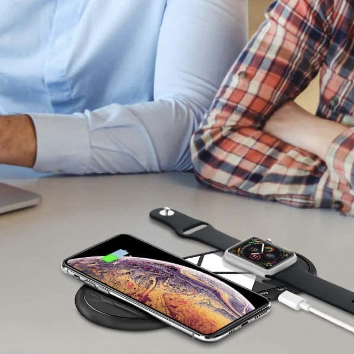 Wireless Charging 桌布 壁紙 — 兩個人坐在辦公桌前，一部智能手機和智能手錶正在黑色充電板上無線充電。