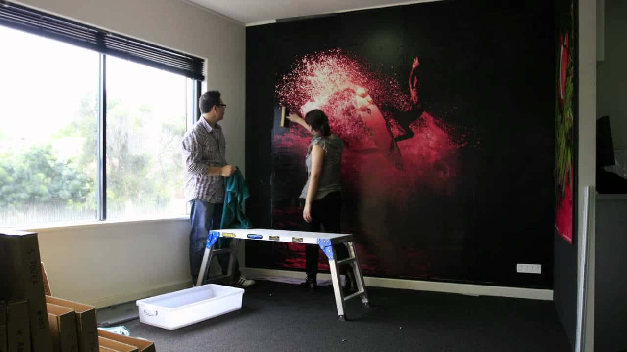Installation Art 桌布 壁紙 — 兩個人正在一個現代房間內安裝一幅充滿活力的紅黑抽象牆紙，其設計帶有動態的潑濺效果。