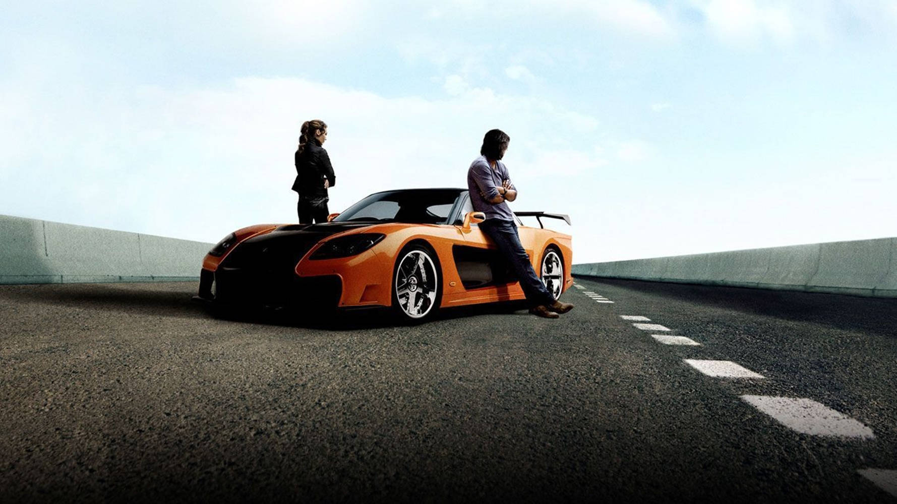 Sports Car 桌布 壁紙 — 兩個人站在一輛鮮橙色跑車旁邊，該車停泊在陽光普照的高速公路上，設有混凝土護欄和晴朗的藍天。