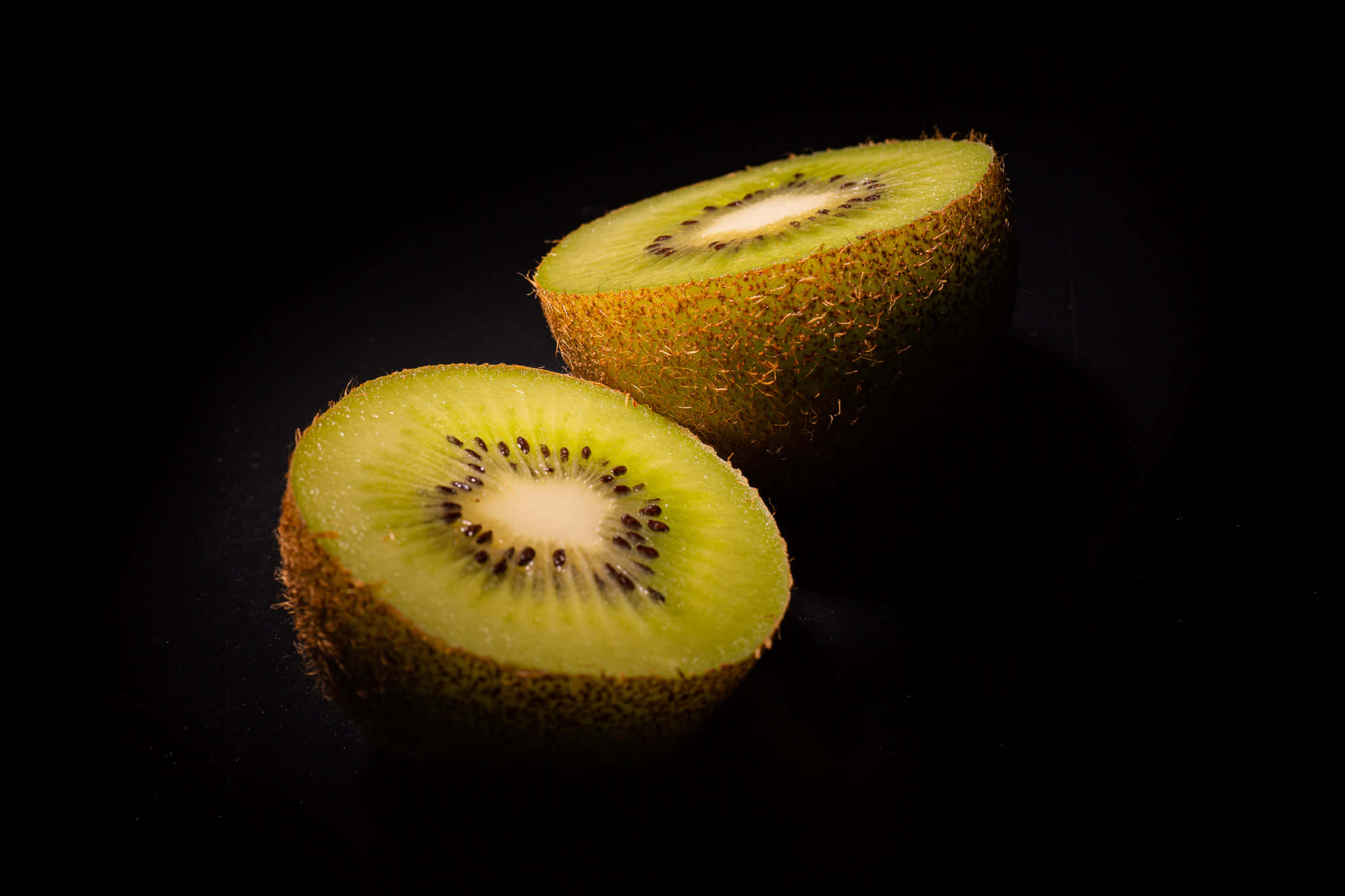 Kiwi 桌布 壁紙 — 兩個切開一半的奇異果，在純黑背景下露出多汁的綠色果肉和黑色種子。