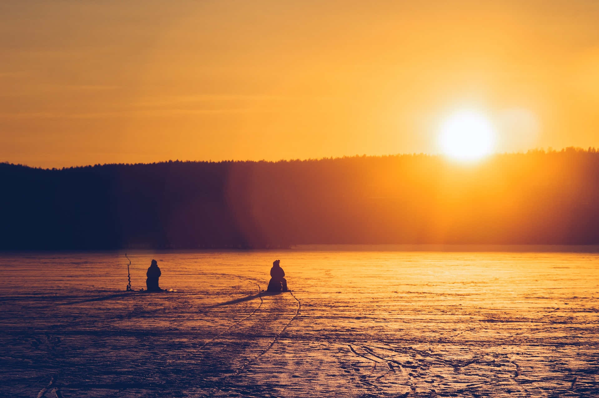 Ice Fishing 桌布 壁紙 — 兩個剪影人物在結冰的湖上冰釣，夕陽如火般橙金交織。