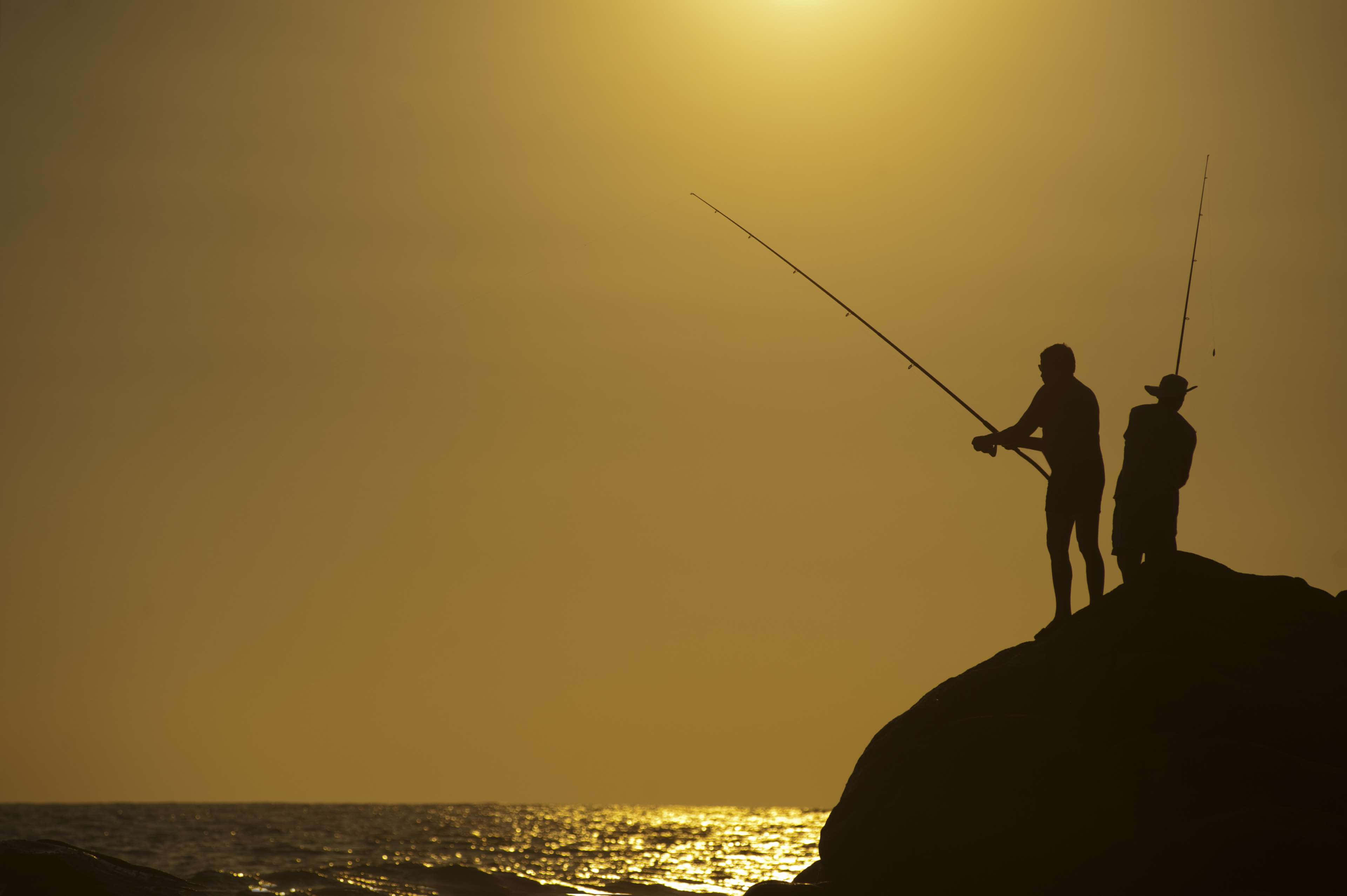 Fishing Rod 桌布 壁紙 — 兩個剪影漁夫企喺岩石懸崖上，喺金色迷霧中嘅日落時分將魚線拋入海洋。