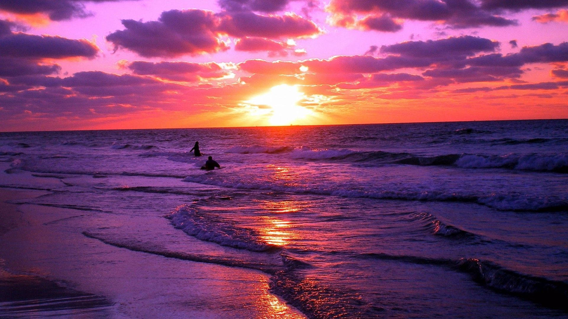 Aesthetic Sunset 桌布 壁紙 — 兩個剪影的衝浪者在火熱的粉紅色和橙色日落天空下乘風破浪。