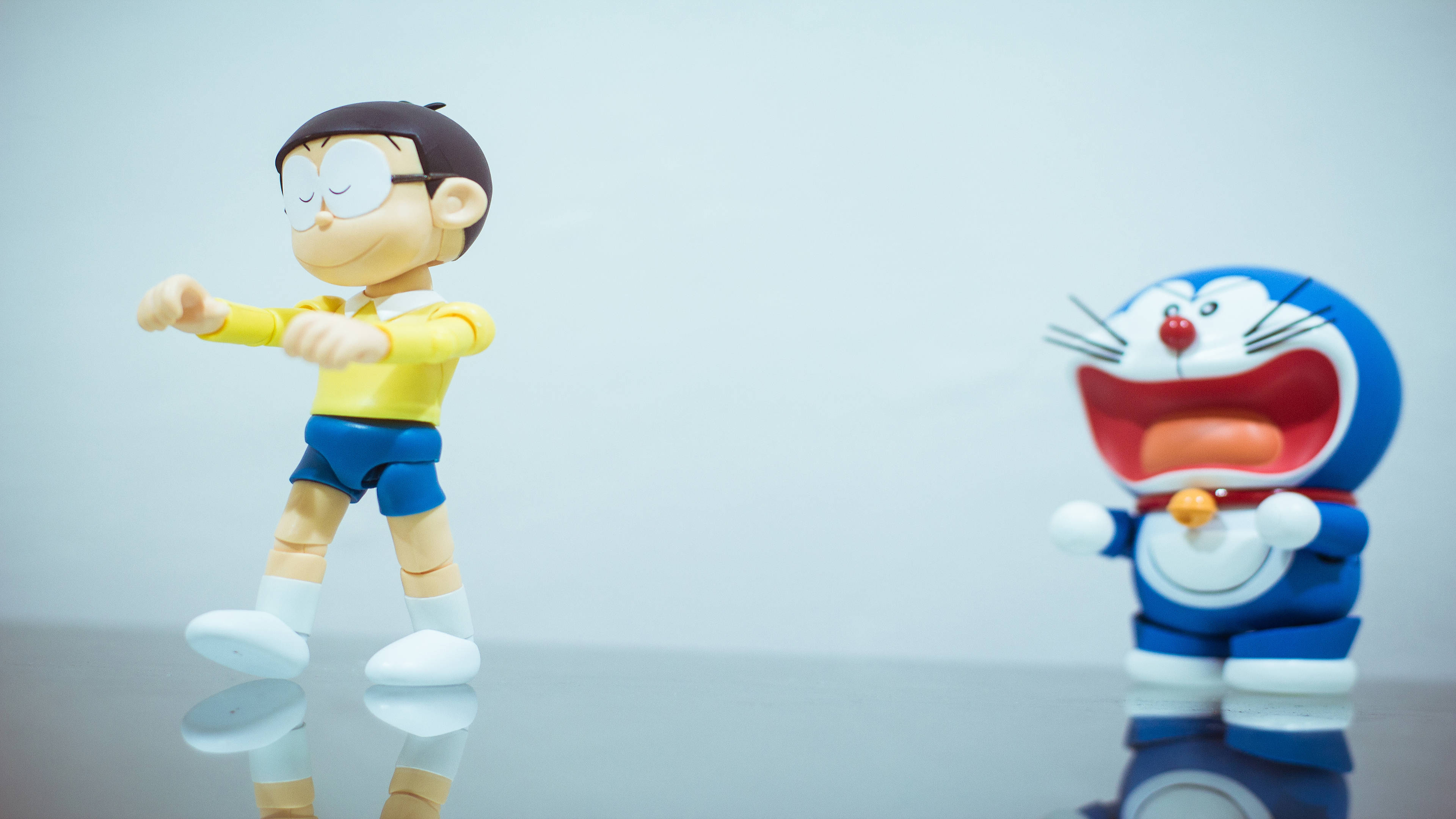 Doraemon 桌布 壁紙 — 兩個動漫公仔多啦A夢和大雄在純色背景前的反光表面上擺姿勢。