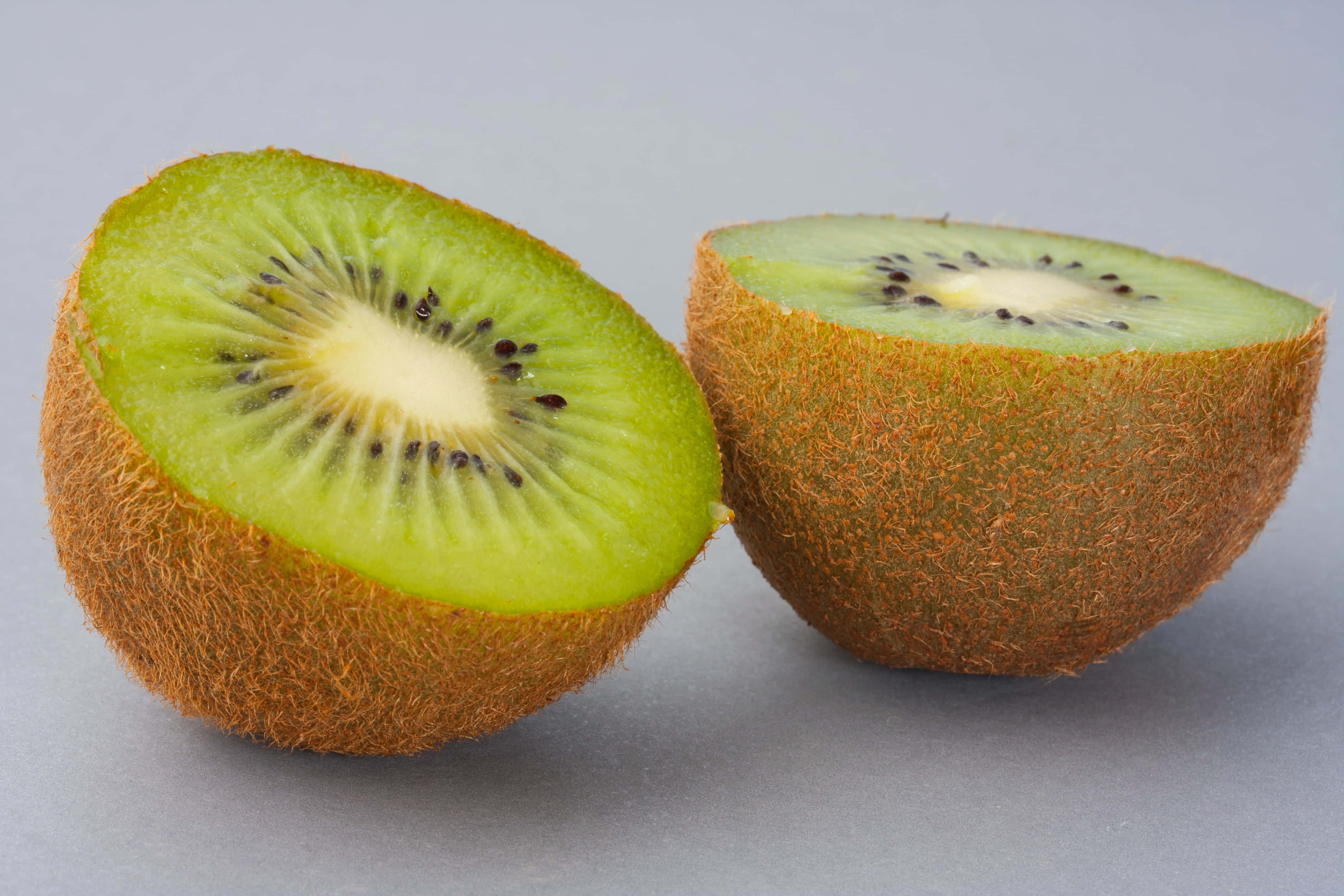 Kiwi 桌布 壁紙 — 兩個半邊奇異果切開，露出鮮綠色果肉和黑色種子，背景為中性灰色。