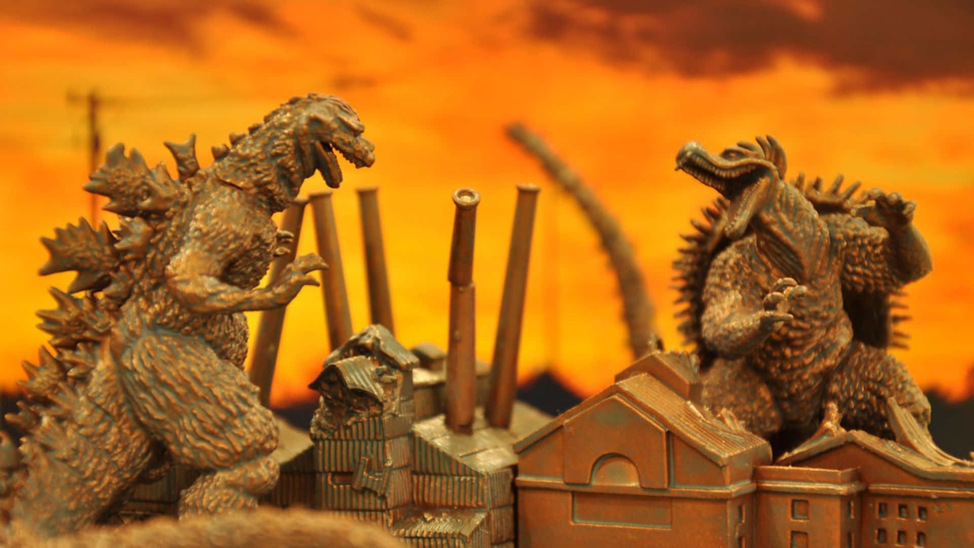 Godzilla Vs Anguirus 桌布 壁紙 — 兩個哥斯拉公仔喺火辣辣橙色日落天空下嘅微型建築物頂部碰撞。