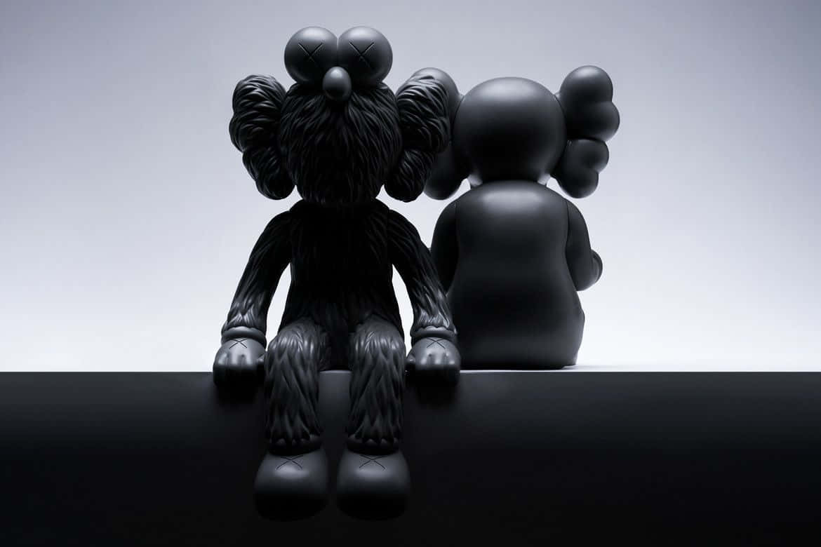 Kaws Bff Black 桌布 壁紙 — 兩個啞光黑色KAWS人偶並排坐在光滑的黑色壁架上，背景為漸變灰色。