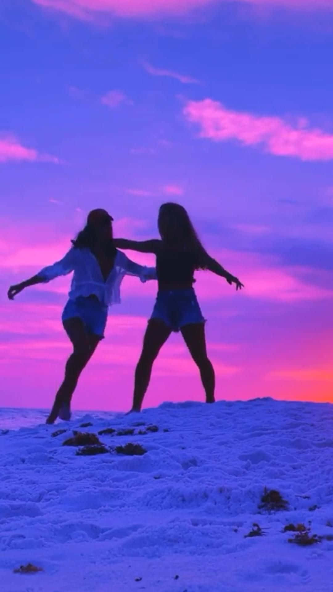 兩個女孩在日落時分站在沙灘上 壁紙