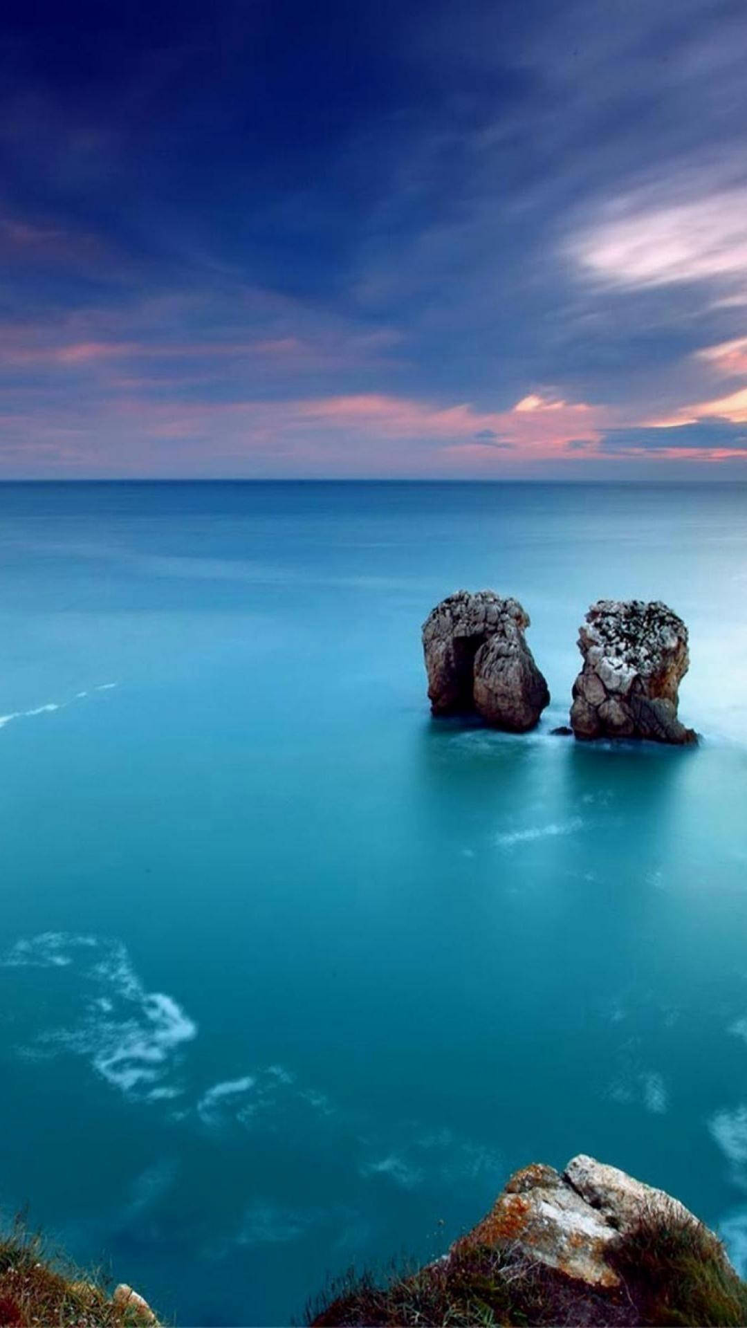 Sea 桌布 壁紙 — 兩個崎嶇的海蝕柱從碧綠的海水中升起，在戲劇性的暮色天空下，天空佈滿粉紅色和深藍色的雲彩。