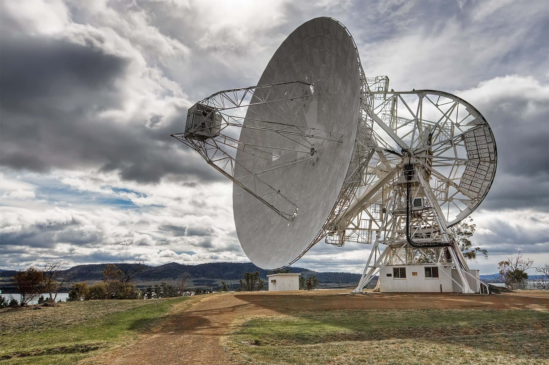 Radio Telescope 桌布 壁紙 — 兩個巨大的衛星天線聳立在戲劇性的多雲天空下，俯瞰遠處的湖泊和山丘。