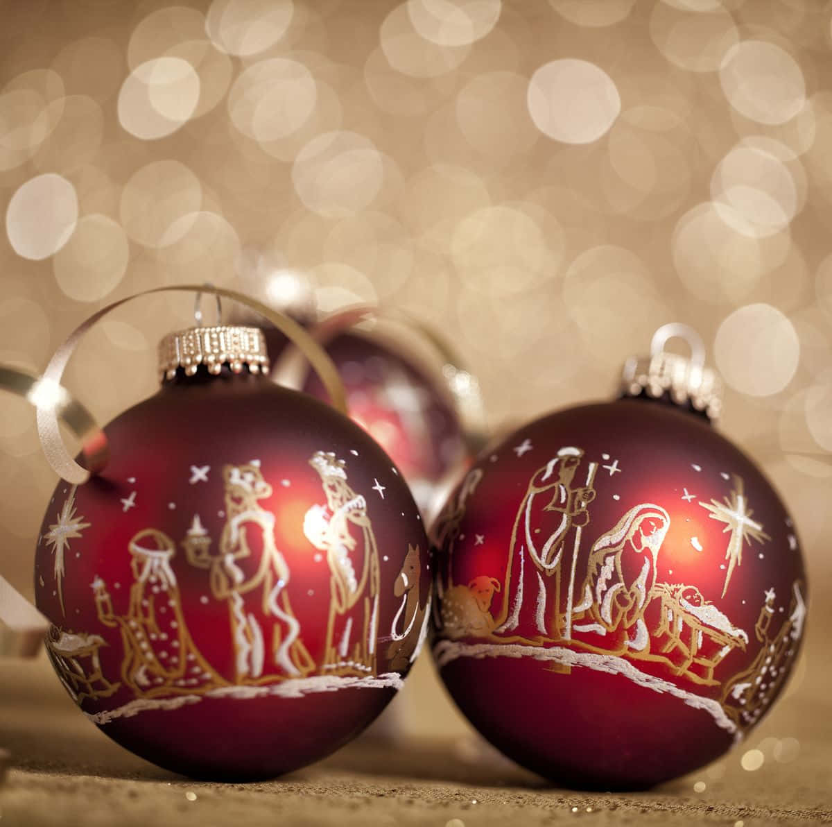 Christmas Eve 桌布 壁紙 — 兩個帶有金色耶穌誕生場景的光滑紅色聖誕裝飾在溫暖的散景背景中閃耀。