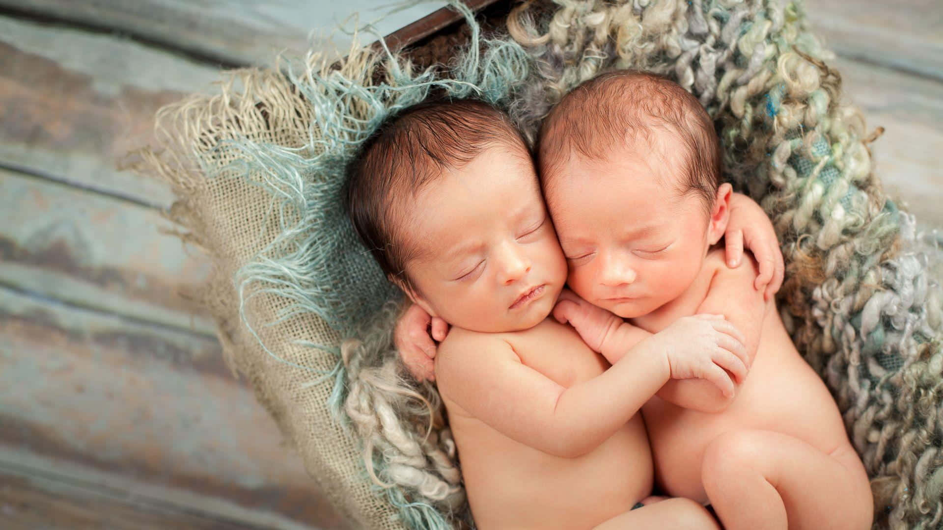 Cute Babies 桌布 壁紙 — 兩個平靜的新生雙胞胎依偎在一個柔軟有質感的籃子裡，放在質樸的木質表面上睡覺。