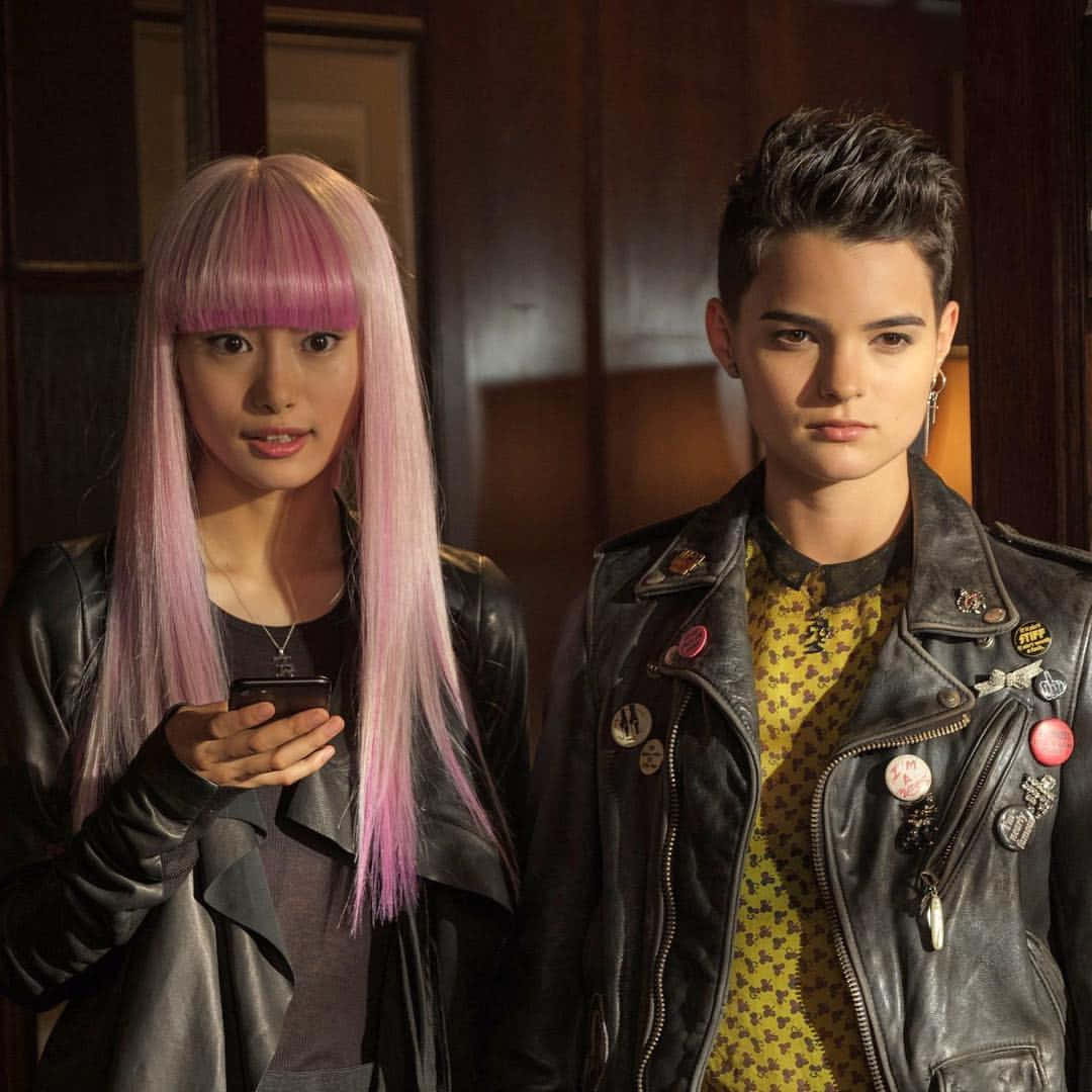 Negasonic Teenage Warhead 桌布 壁紙 — 兩個年輕人留著大膽的粉紅色頭髮，穿著皮褸，站在室內，其中一人拿著手機，兩人都表情嚴肅。