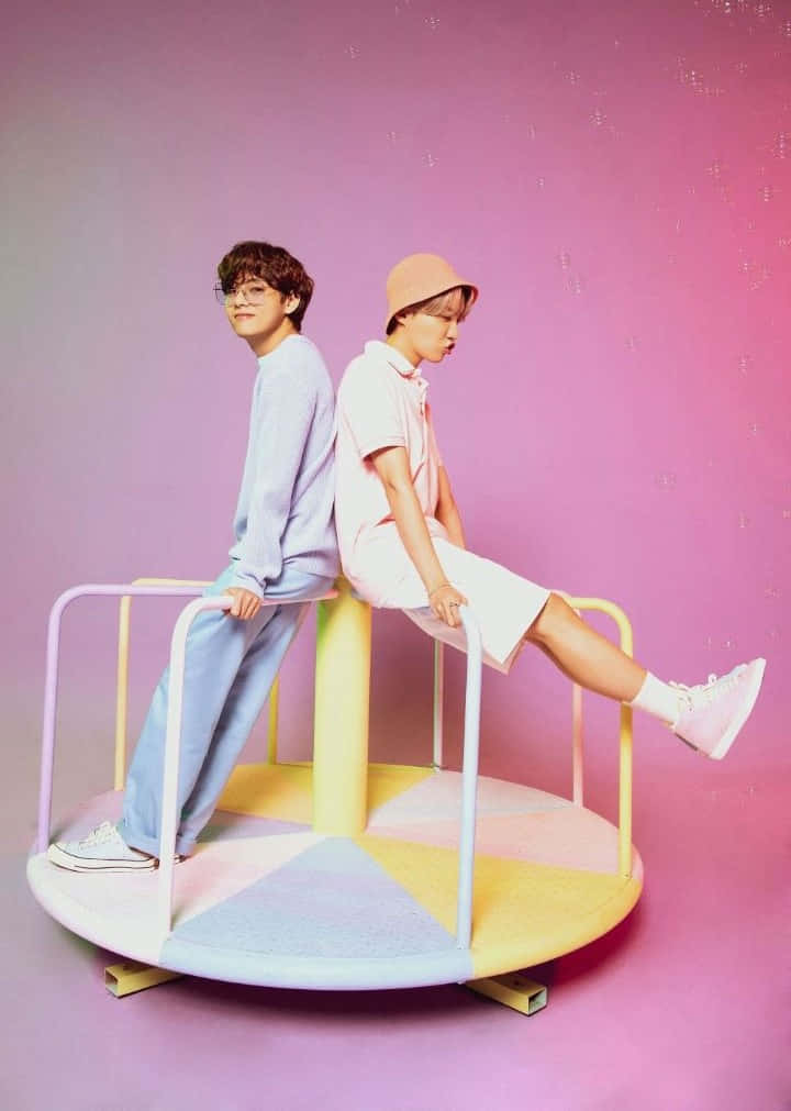 Big Hit Entertainment 桌布 壁紙 — 兩個年輕人背對背坐在色彩繽紛的旋轉木馬座位上，背景是柔和的粉紅色漸變。