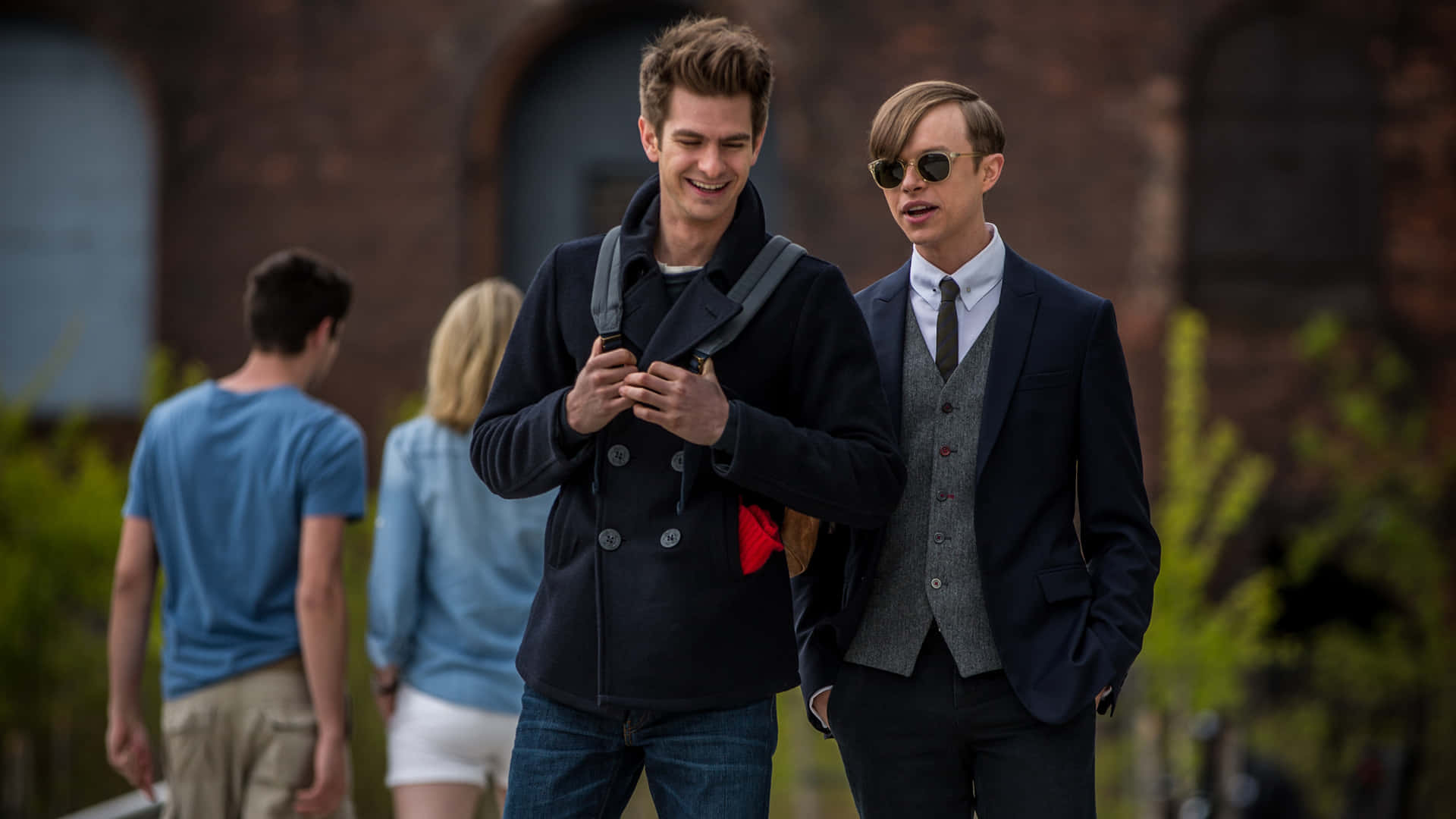 Harry Osborn 桌布 壁紙 — 兩個年輕男子在校園小徑上同行，其中一個邊笑邊調整背包，另一個戴著太陽眼鏡和西裝。