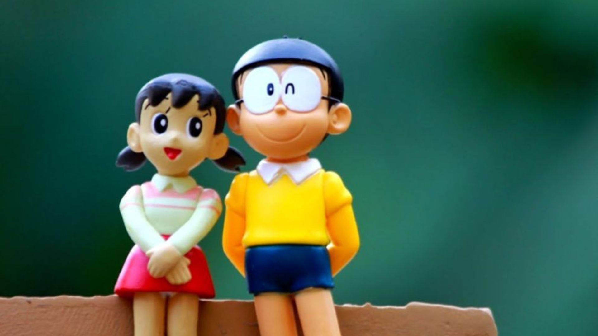 shizuka doraemon 桌布 壁紙 — 兩個微笑的動漫風格多啦A夢和靜香公仔並排坐在木製架子上，背景是柔和的綠色。