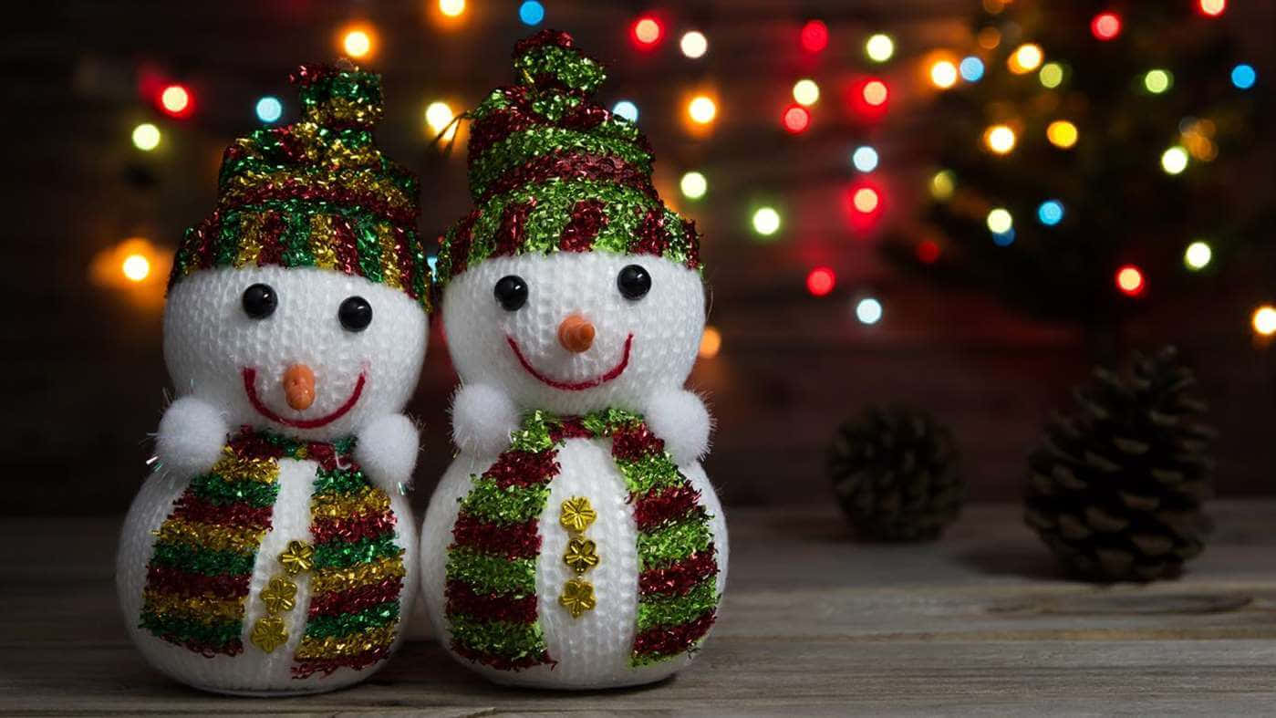 Winter Holiday 桌布 壁紙 — 兩個快樂的針織雪人，戴著閃亮的帽子和圍巾，在色彩繽紛的聖誕燈飾散景背景下微笑。