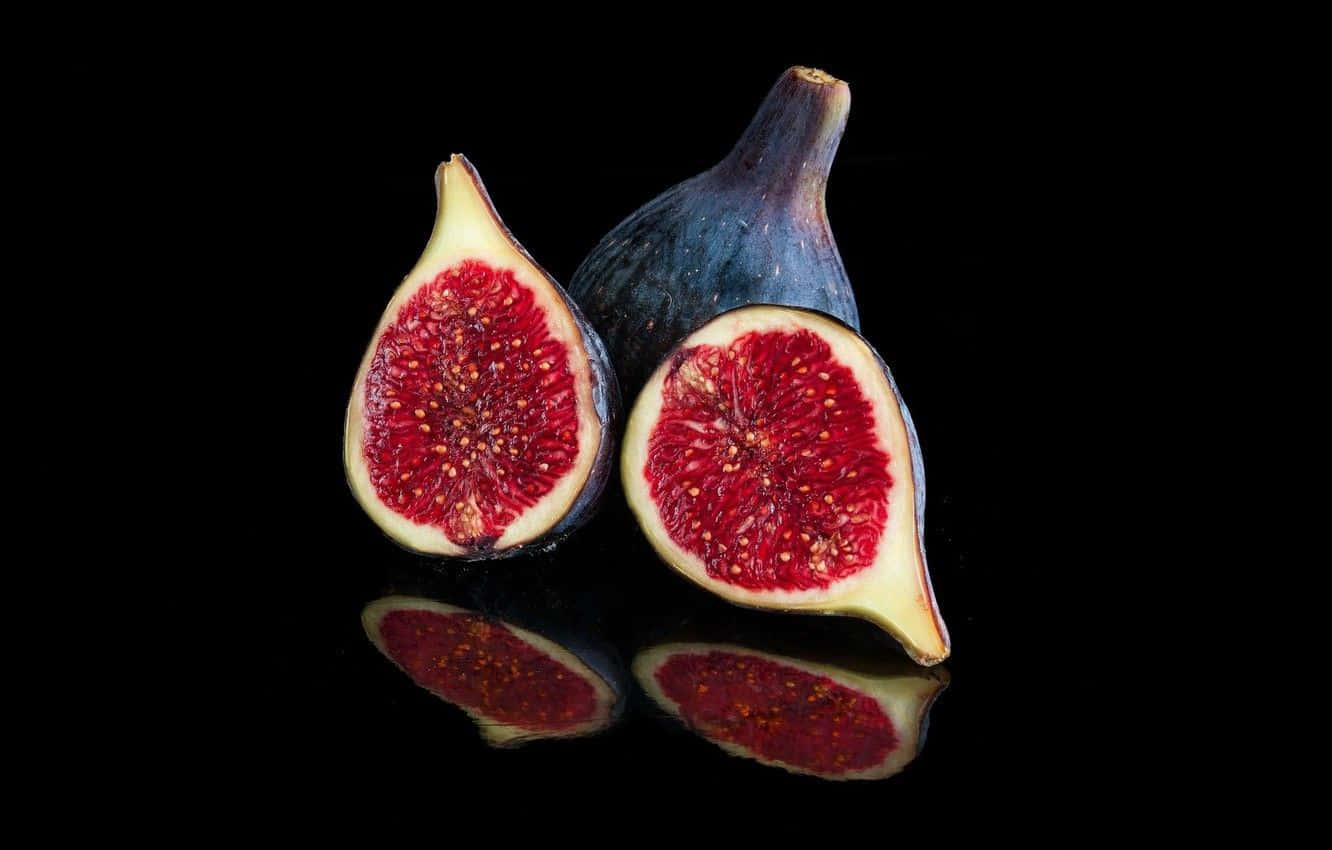 Purple Figs 桌布 壁紙 — 兩個成熟的無花果，一個完整，一個切片，在光滑的黑色反光表面上露出多汁的紅色果肉。