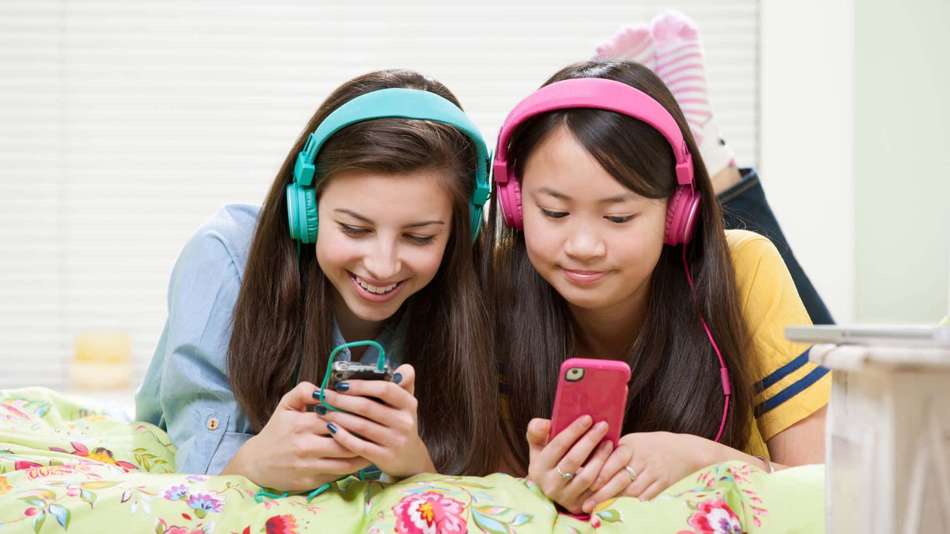 Best Friend 桌布 壁紙 — 兩個戴著彩色耳機的微笑女孩躺在花卉床上，專注於她們的手機。