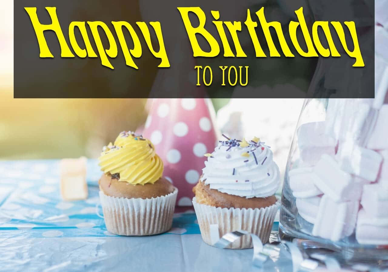 Birthday Wishes 桌布 壁紙 — 兩個有糖霜和彩色糖粒的杯子蛋糕放在藍色圓點桌布上，下方有 'Happy Birthday To You' 橫幅。