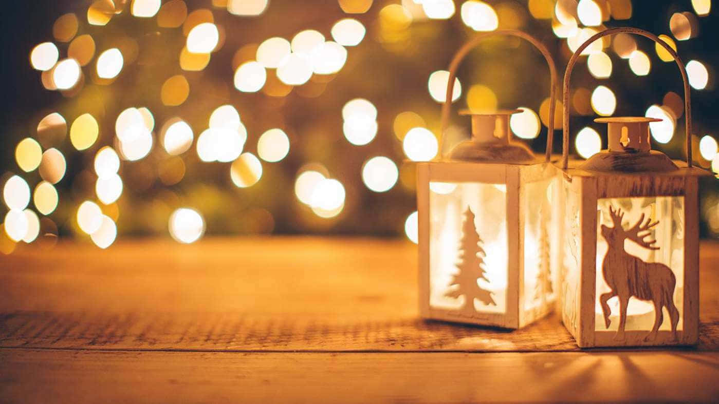 Winter Holiday 桌布 壁紙 — 兩個木製燈籠，帶有鹿和樹木鏤空圖案，在木質表面上溫暖地發光，背景是金色燈光的散景效果。