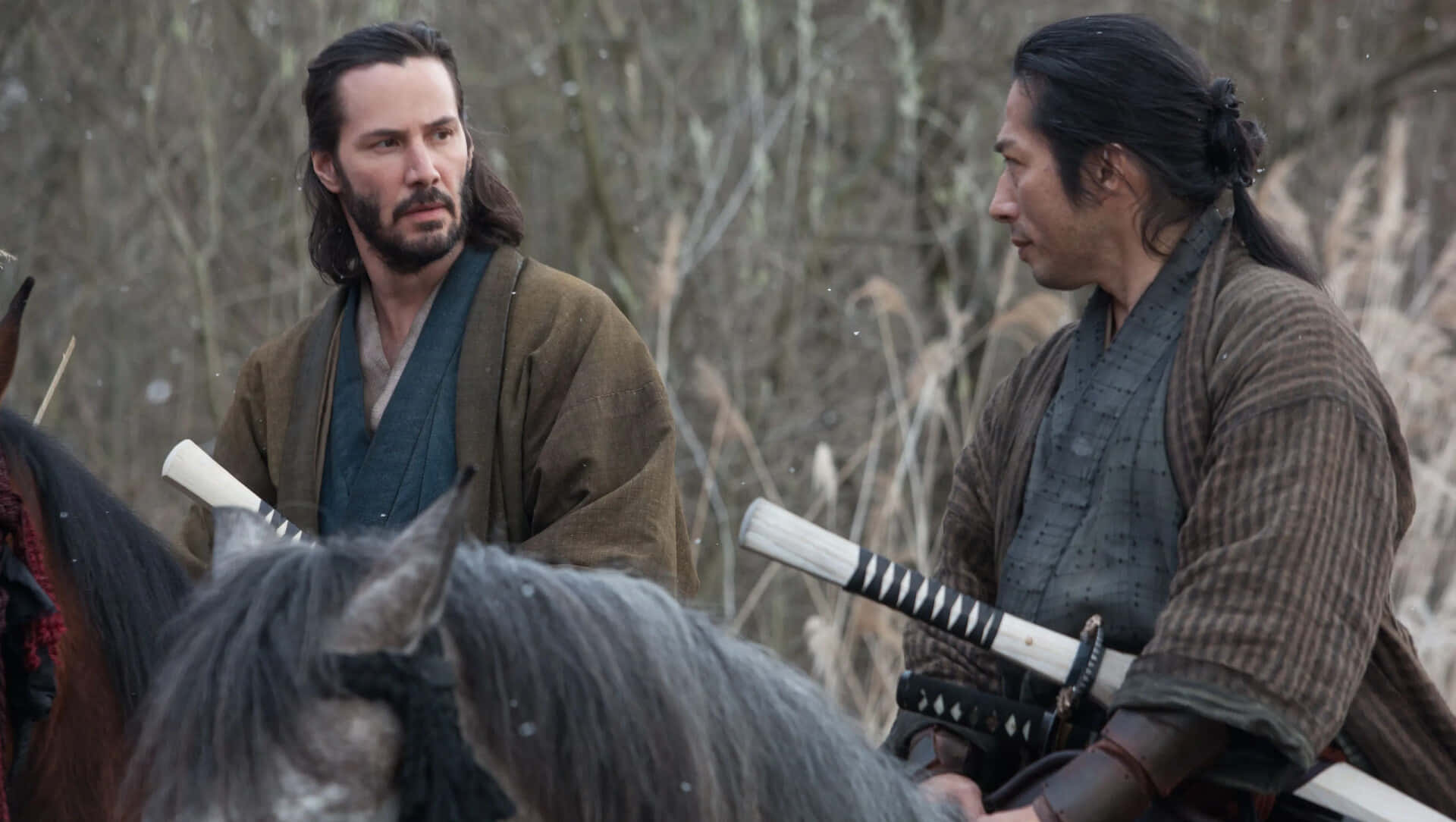 47 Ronin 桌布 壁紙 — 兩個武士騎著馬，在白雪覆蓋的森林空地中，表情緊張，拔劍相對。