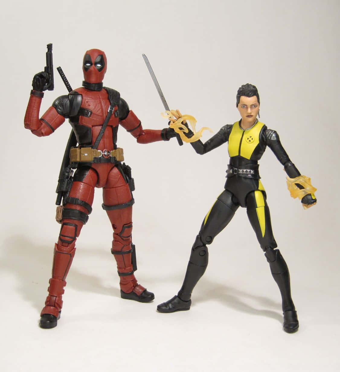 Deadpool And Negasonic Teenage Warhead 桌布 壁紙 — 兩個死侍和多米諾的動作人偶在純白色背景前動態擺姿勢，手持武器。