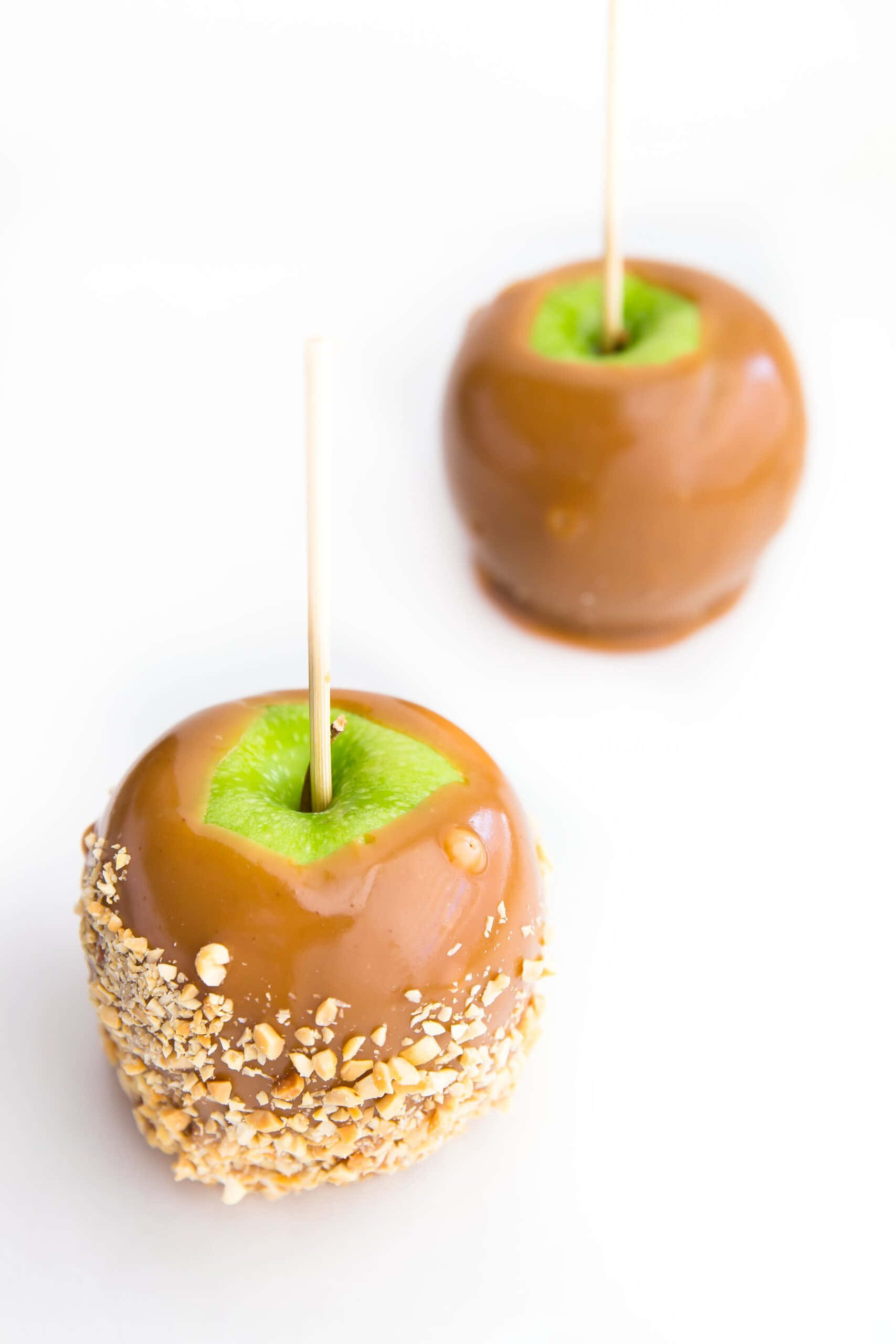 Caramel Apples 桌布 壁紙 — 兩個焦糖塗層蘋果，帶有綠色莖和堅果碎屑塗層，白色背景。