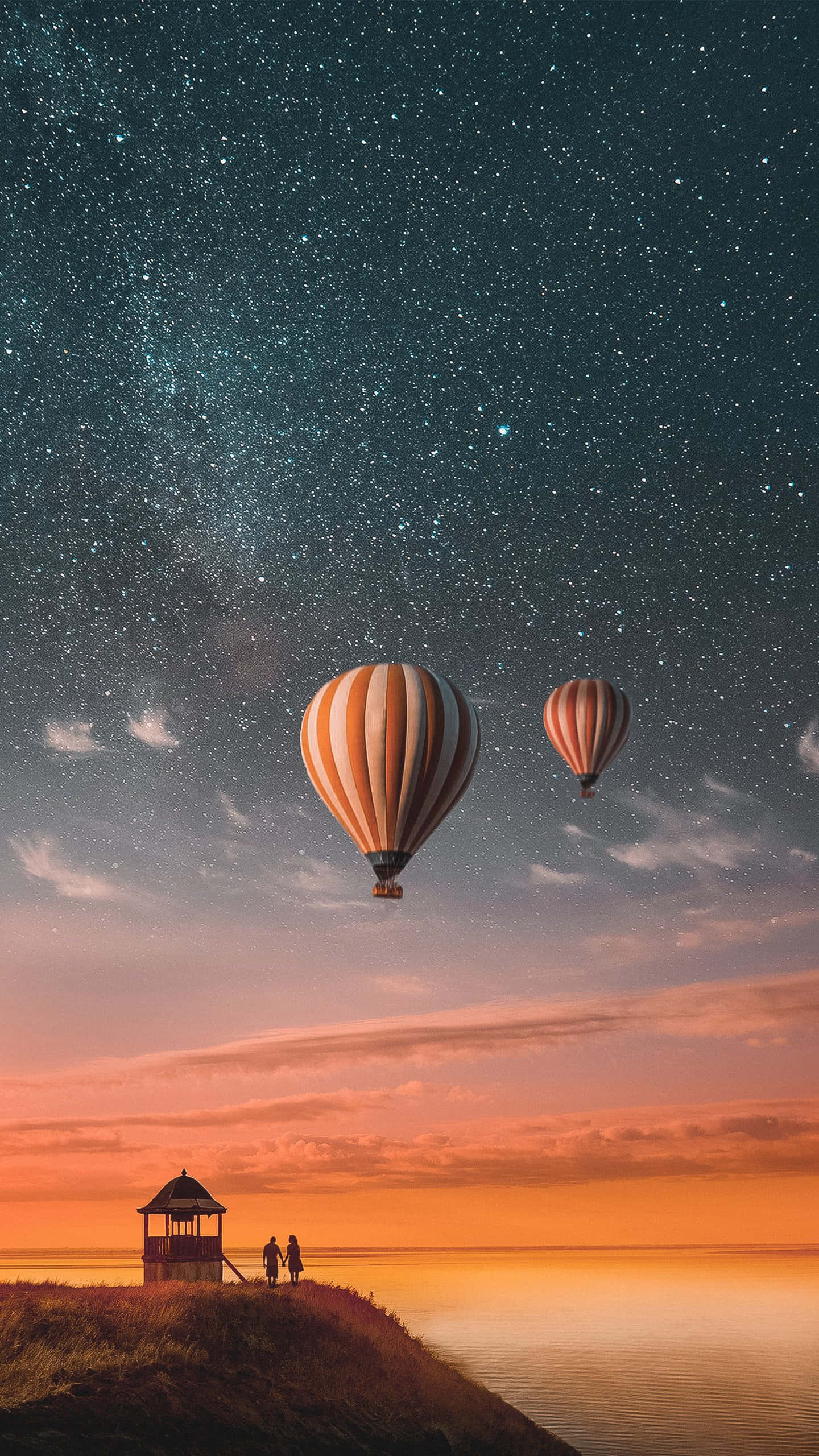Captivating 桌布 壁紙 — 兩個熱氣球在星空下飄浮，位於海邊懸崖上方，懸崖上有兩人在日落時分靠近涼亭站立。