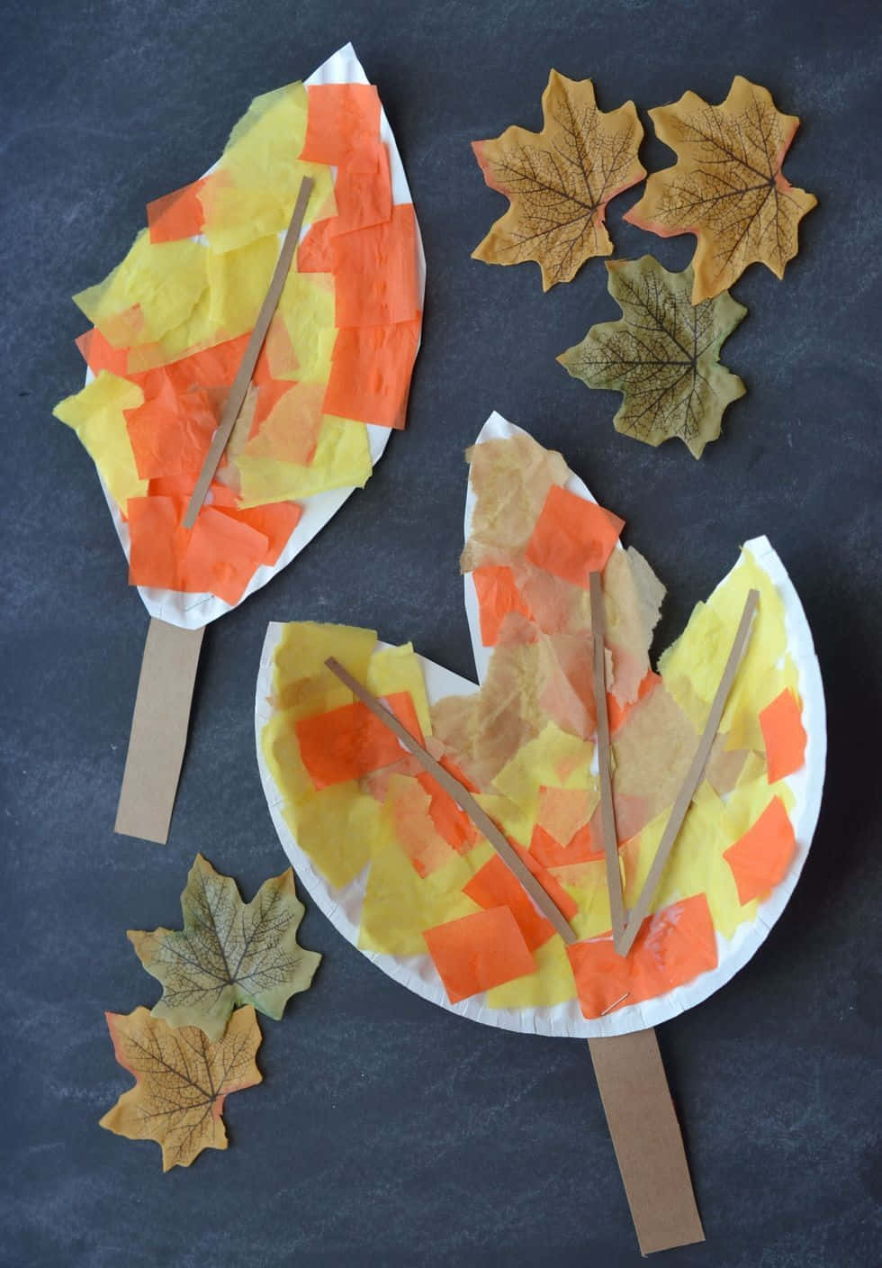 Fall Crafts 桌布 壁紙 — 兩個用紙碟和紙巾製作的手工秋季樹葉工藝品，旁邊放著真正的楓葉，在深灰色表面上。